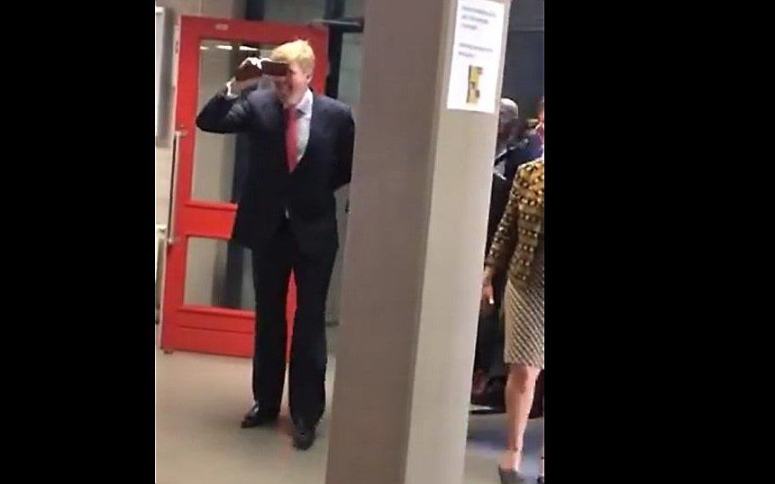 Koning Willem-Alexander reageert op filmende en fotograferende scholieren door zelf ook zijn mobiele telefoon voor zijn gezicht te houden en zijn tong uit te steken. beeld uit video YouTube