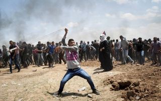 Een Palestijnse betoger slingerde maandag een steen richting Israëlische soldaten bij de grens tussen de Gazastrook en Israël. Bij confrontaties rond de grens zouden gisteren zeker 58 doden zijn gevallen. beeld EPA, Luca Piergiovanni