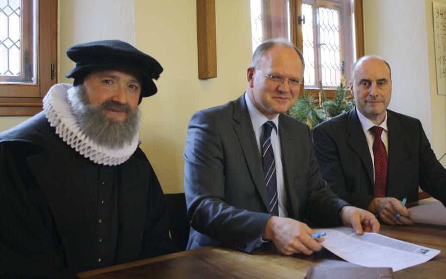 Ondertekening van de overeenkomst tussen Neustadt en Refo 500. V.l.n.r.: ds. Michael Landgraf in de rol van Zacharias Ursinus; prof. dr. Herman Selderhuis, directeur van Refo500; en wethouder Georg Krist van de gemeente Neustadt. Foto Tourist-Information 