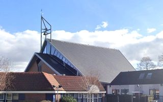 Kerkgebouw met klok; daarvoor andere gebouwen en een auto.