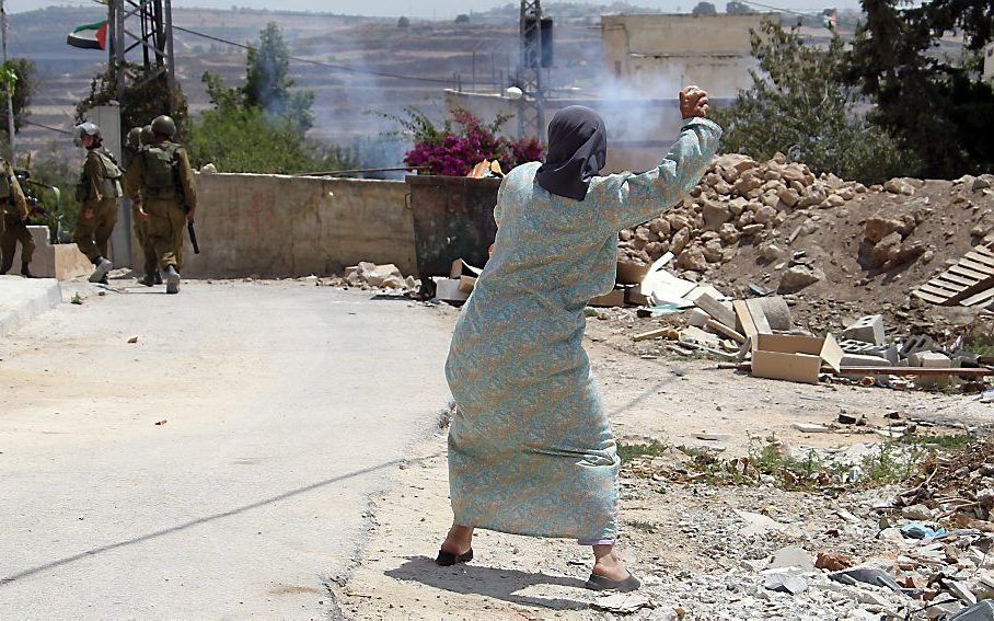 Een Palestijnse vrouw gooit vrijdag een steen naar Israëlische militairen, ergens op de Westelijke Jordaanoever. Israël en de Palestijnen hervatten binnenkort naar alle waarschijnlijkheid het vredesoverleg. Foto EPA