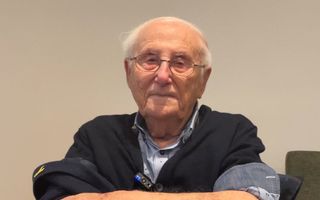 Portretfoto van 100-jarige, man met weinig haar en bril op, armen ontbloot.