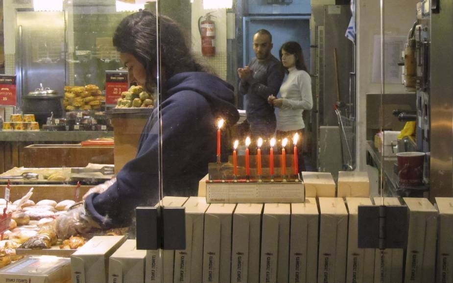 De chanoekakandelaar voor het raam van een bakkerij met sufganiyot. Beeld Alfred Muller