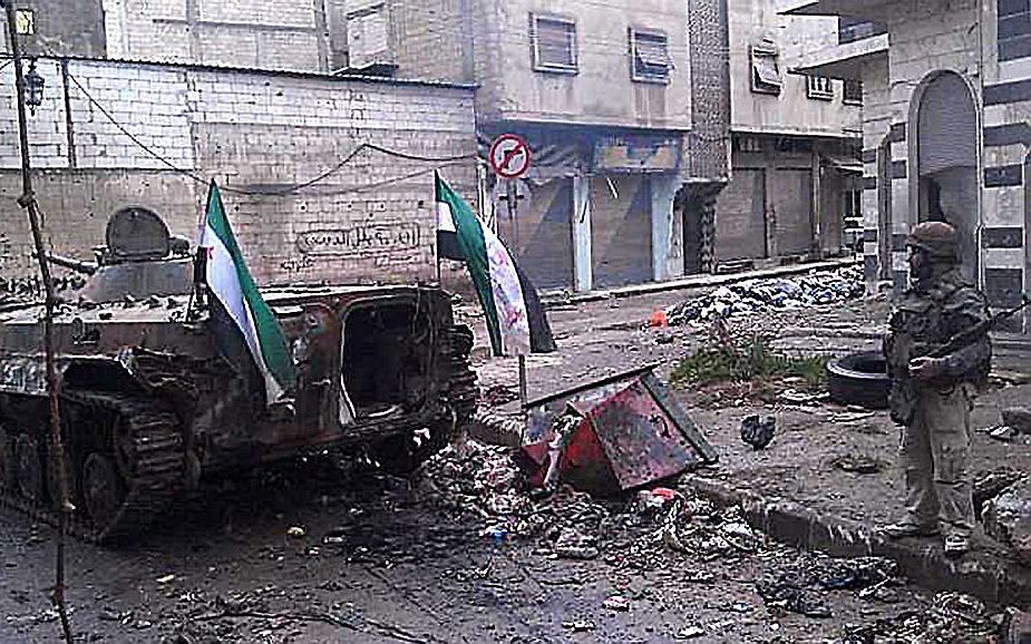 Syrische rebel naast kapotgeschoten tank in Homs. Foto EPA