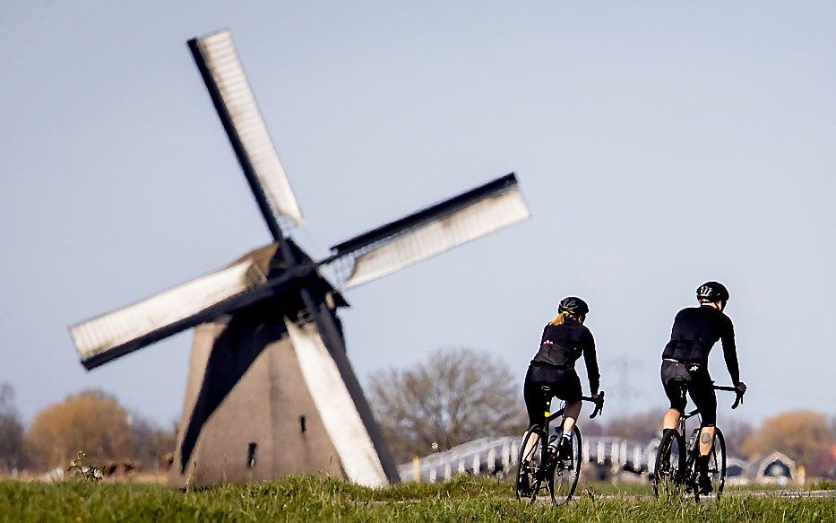 Wielrenners passeren een molen op een dijkje bij Schermerhorn. Veel mensen wielrennen omdat er door het corona-virus minder gesport kan worden. beeld ANP