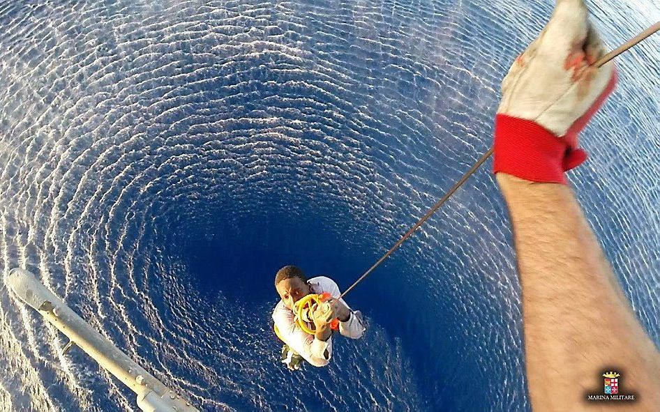 Een migrant wordt maandag per helikopter van een boot van de Italiaanse marine gehaald. Veel Afrikaanse migranten proberen via de Middellandse Zee Europa te bereiken. Beeld AFP