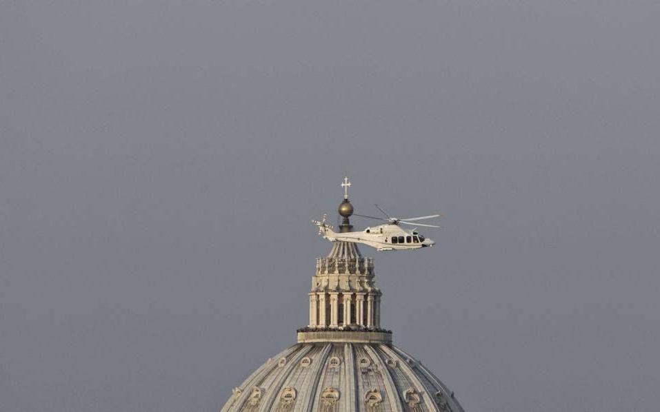 De helikopter van de Italiaanse luchtmacht met daarin de vertrekkende paus stijgt langzaam op en vliegt weg, langs de koepel van de Sint-Pieter. Foto EPA