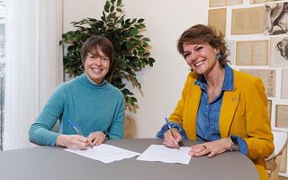 Twee vrouwen zitten aan een tafel, met papieren voor zich en een pen in de hand.