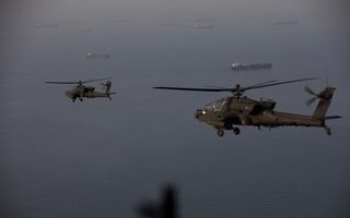 Twee helikopters vliegen boven zee, waar schepen varen.