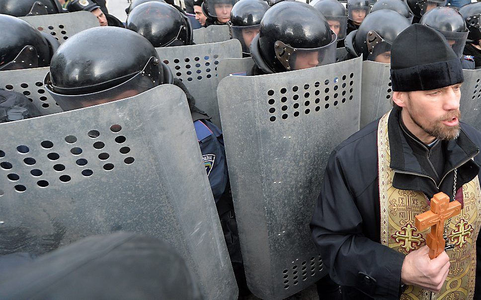 Een priester tussen de demonstranten en de politie in Kiev. Foto AFP