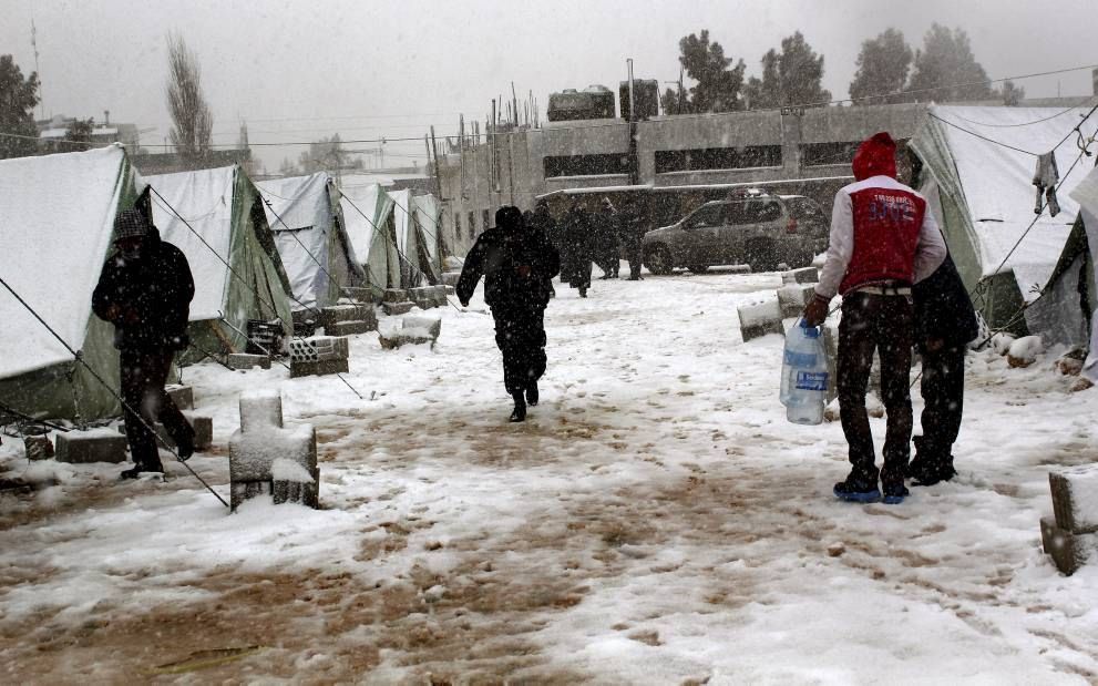 AL-MARJ – Syrische vluchtelingen in een tentenkamp in Libanon wapenen zich tegen de kou. De mannen dragen water naar de tenten, die zijn opgesteld bij het dorp al-Marj in de Bekaavallei in Libanon. Volgens de Verenigde Naties zijn ruim 150.000 Syriërs inm