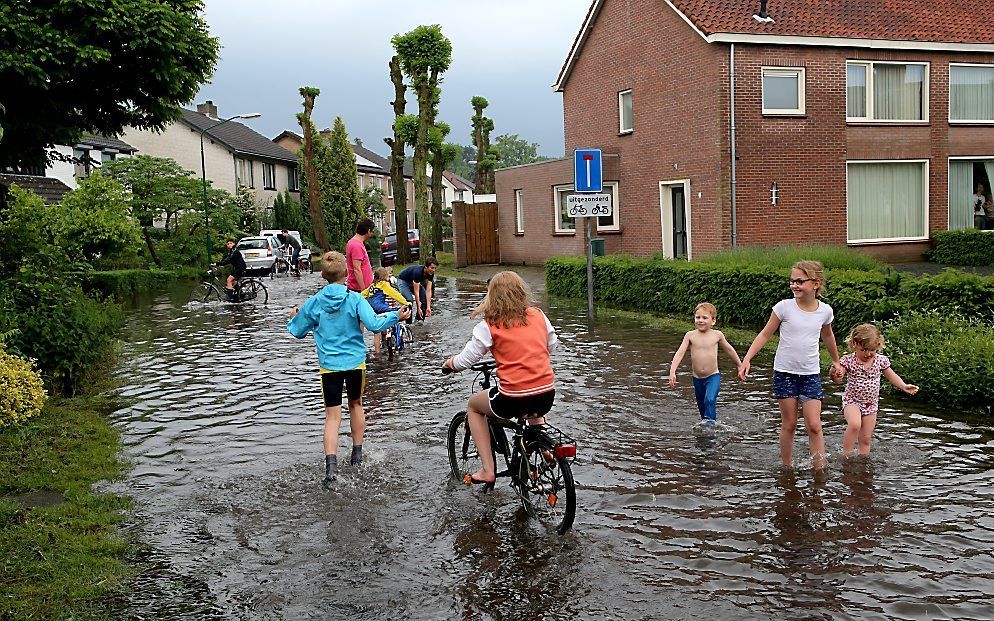 Kinderen in een ondergelopen straat afgelopen woensdag. Op verschillende plaatsen in het oosten van Noord-Brabant en het noorden van Limburg hebben hoosbuien wateroverlast veroorzaakt. beeld ANP