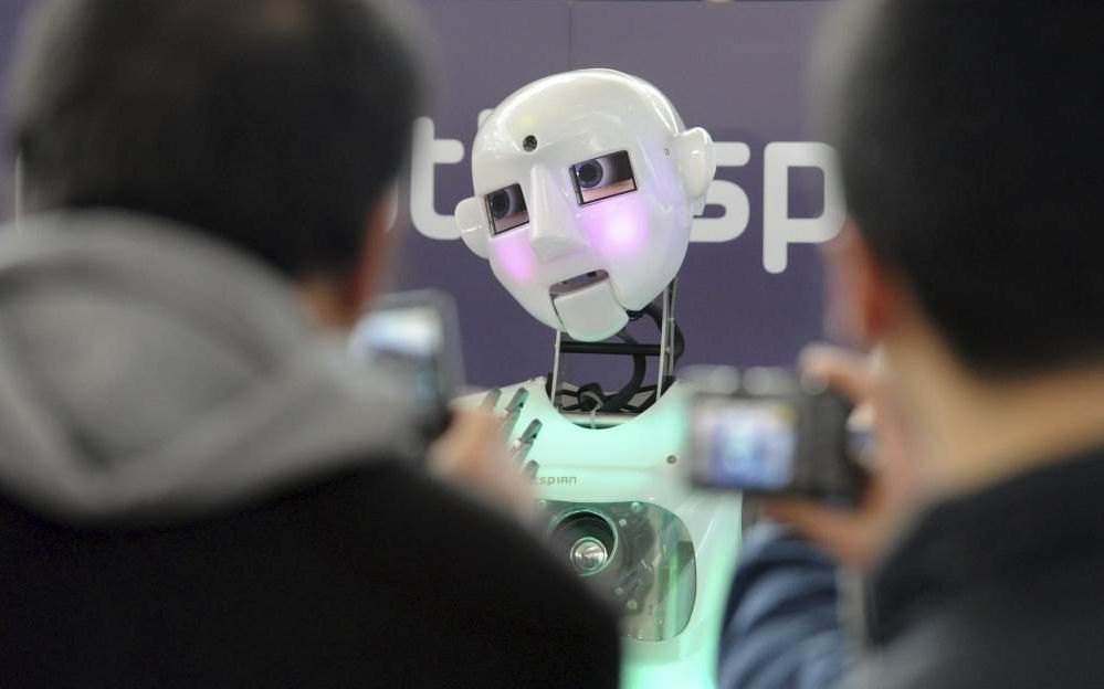 Bezoekers van ict-beurs Cebit in Hannover bekijken een robot die contact kan maken met mensen. Foto EPA