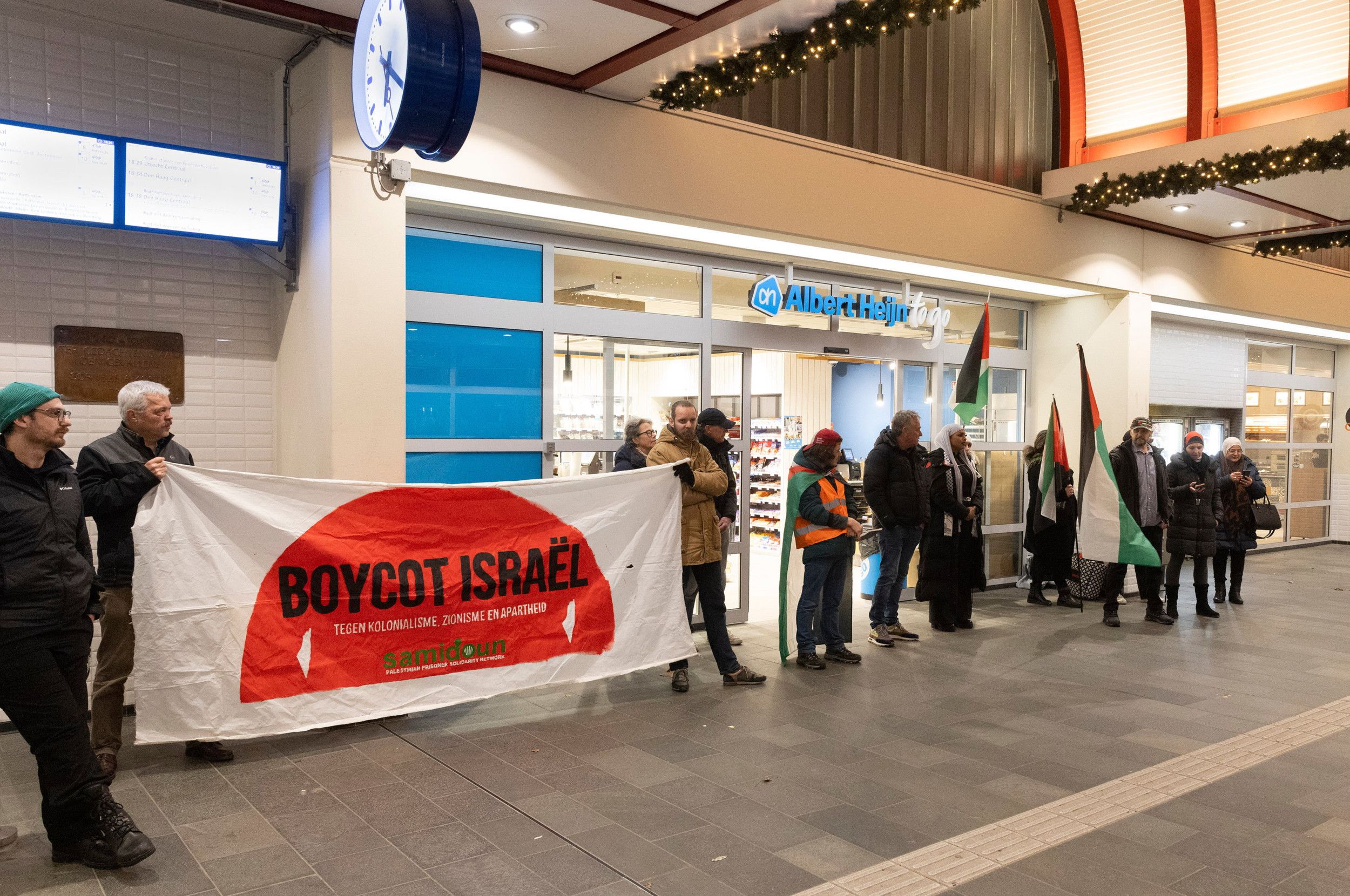 Demonstranten met Palestijnse vlaggen en spandoek ‘Boycot Israël’ bij de ingang van Albert Heijn op het station van Gouda.