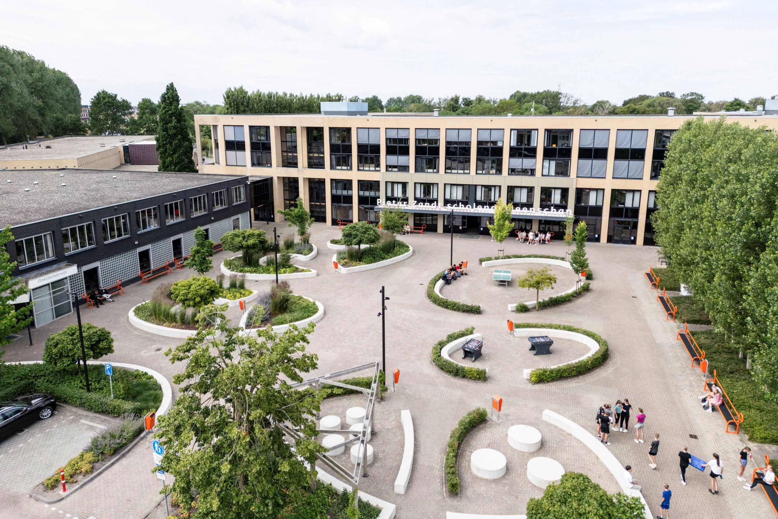 Op het schoolplein van de Pieter Zandt staan witte bankjes in een soort ovaal. Er groeien bomen en bosjes op het plein.