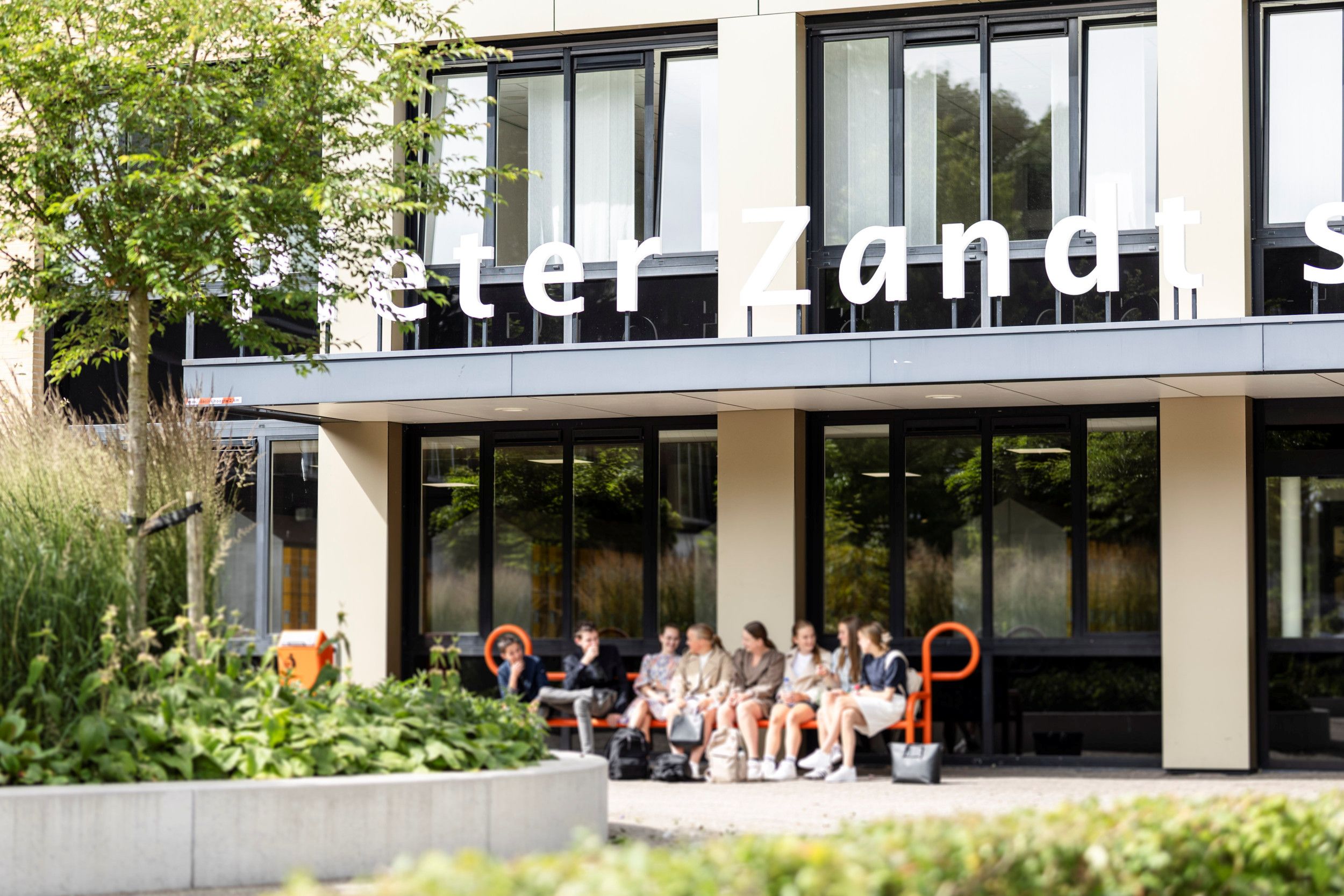 Leerlingen zitten op bankjes voor de Pieter Zandt scholengemeenschap