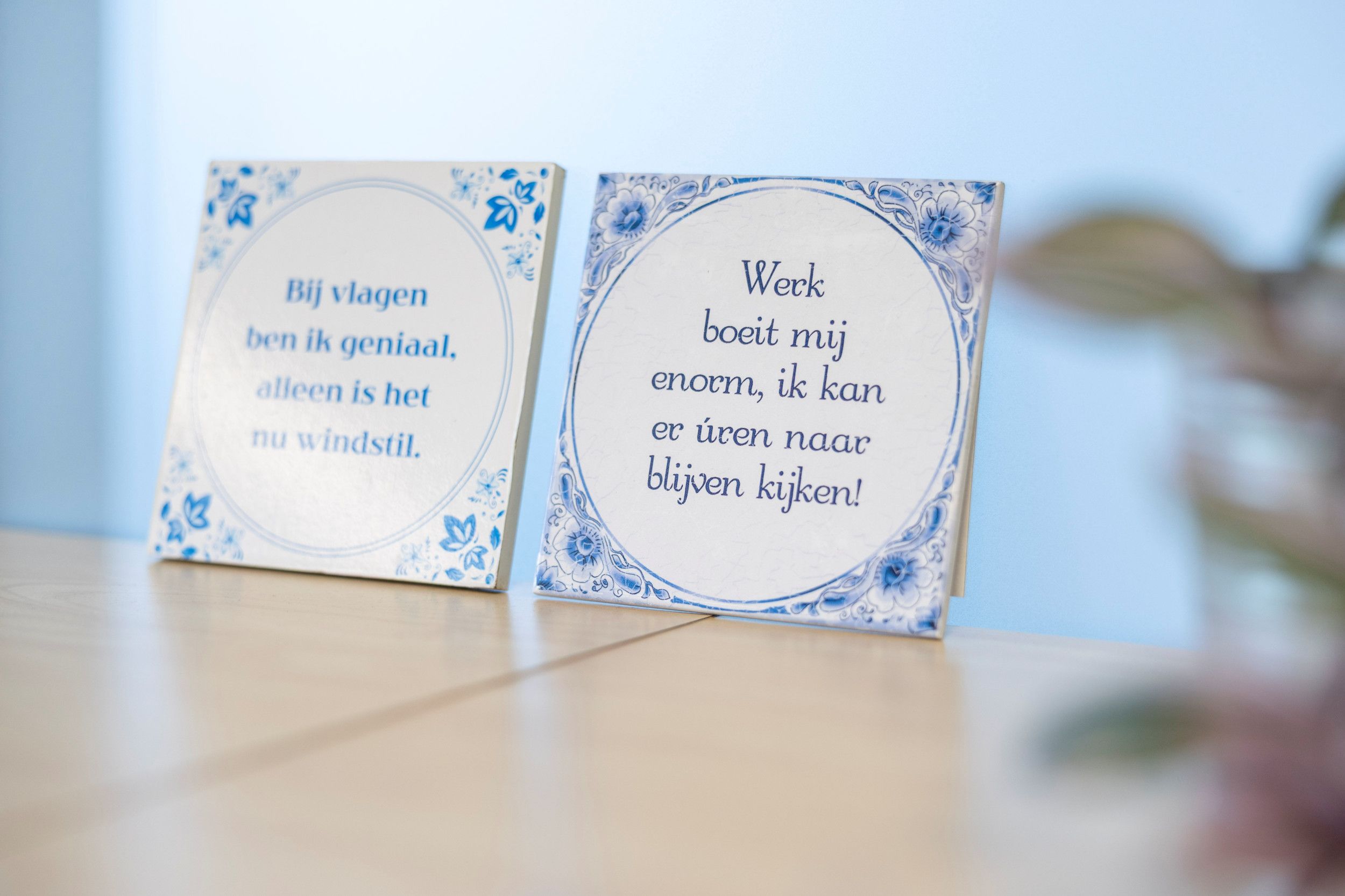 Twee oud-Hollandse tegeltjes met daarop de teksten: „Bij vlagen ben ik geniaal. Alleen is het nu windstil.” en „Werk boeit mij enorm, ik kan er úren naar blijven kijken!”