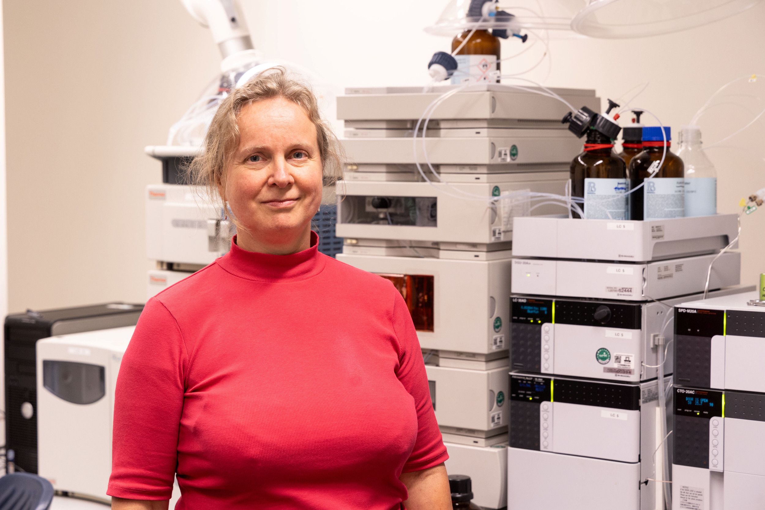 Een vrouw in een rode trui staat voor laboratoriumapparatuur. 