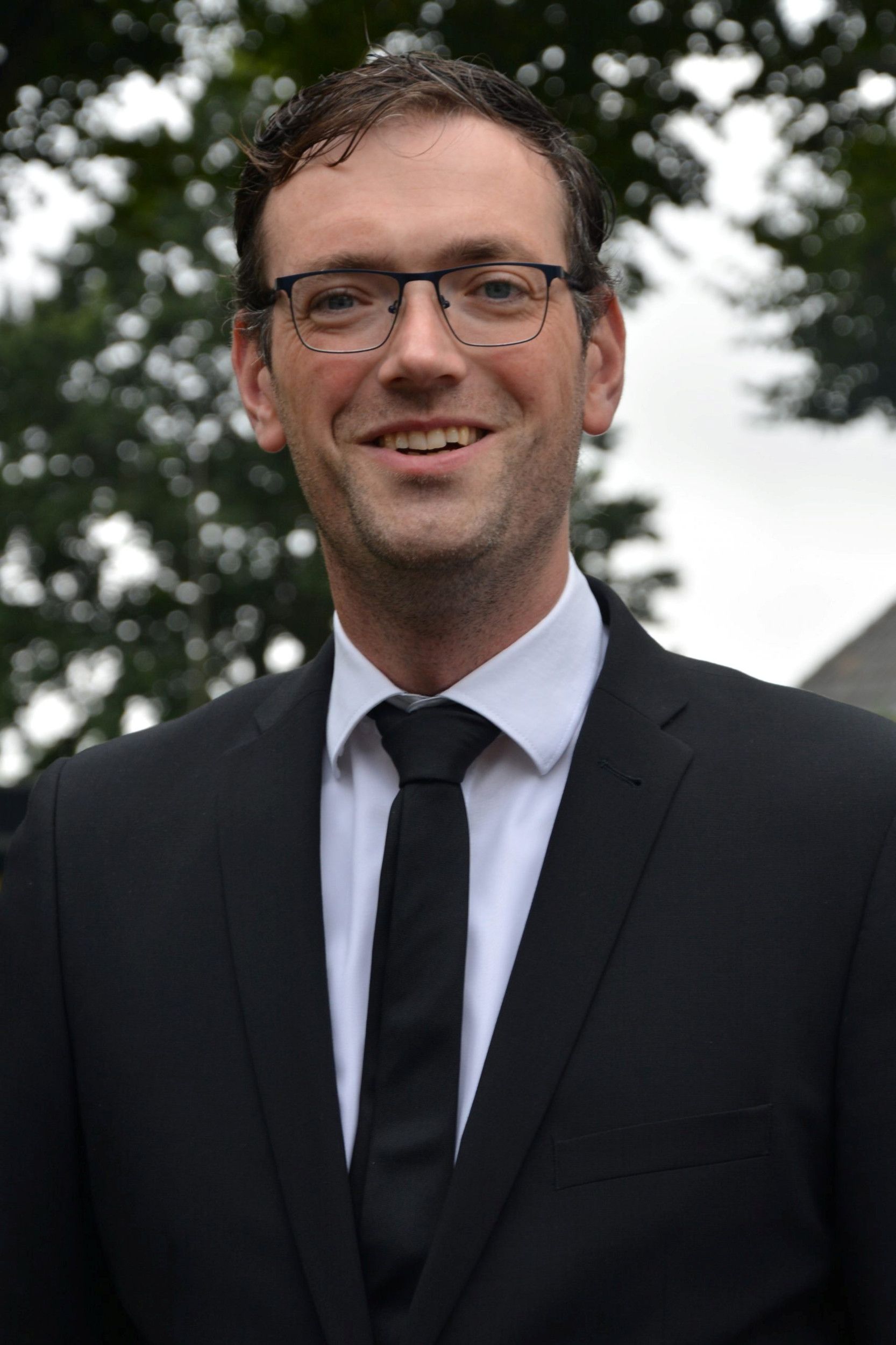 Man in zwart pak en dito stropdas, lachend.