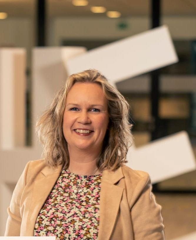 Vrouw met donkerblond haar en een crèmekleurig jasje aan.