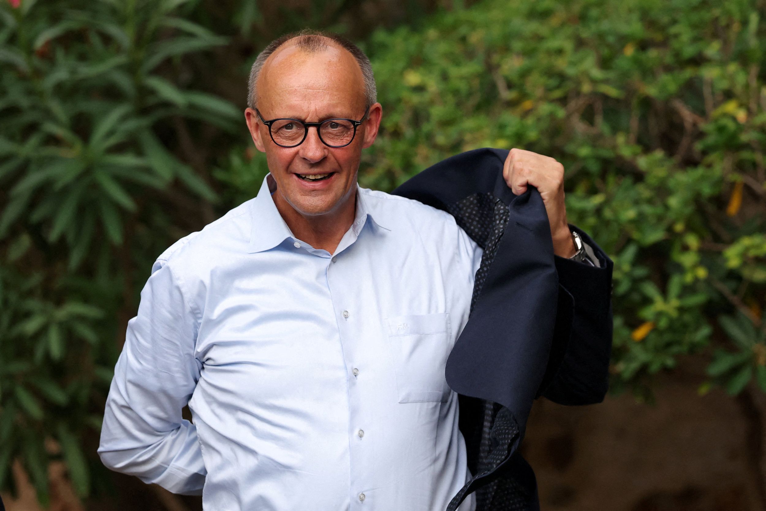 Bondskanselier Merz, een man met een kalend hoofd en een donkere bril, trekt zijn jasje aan.