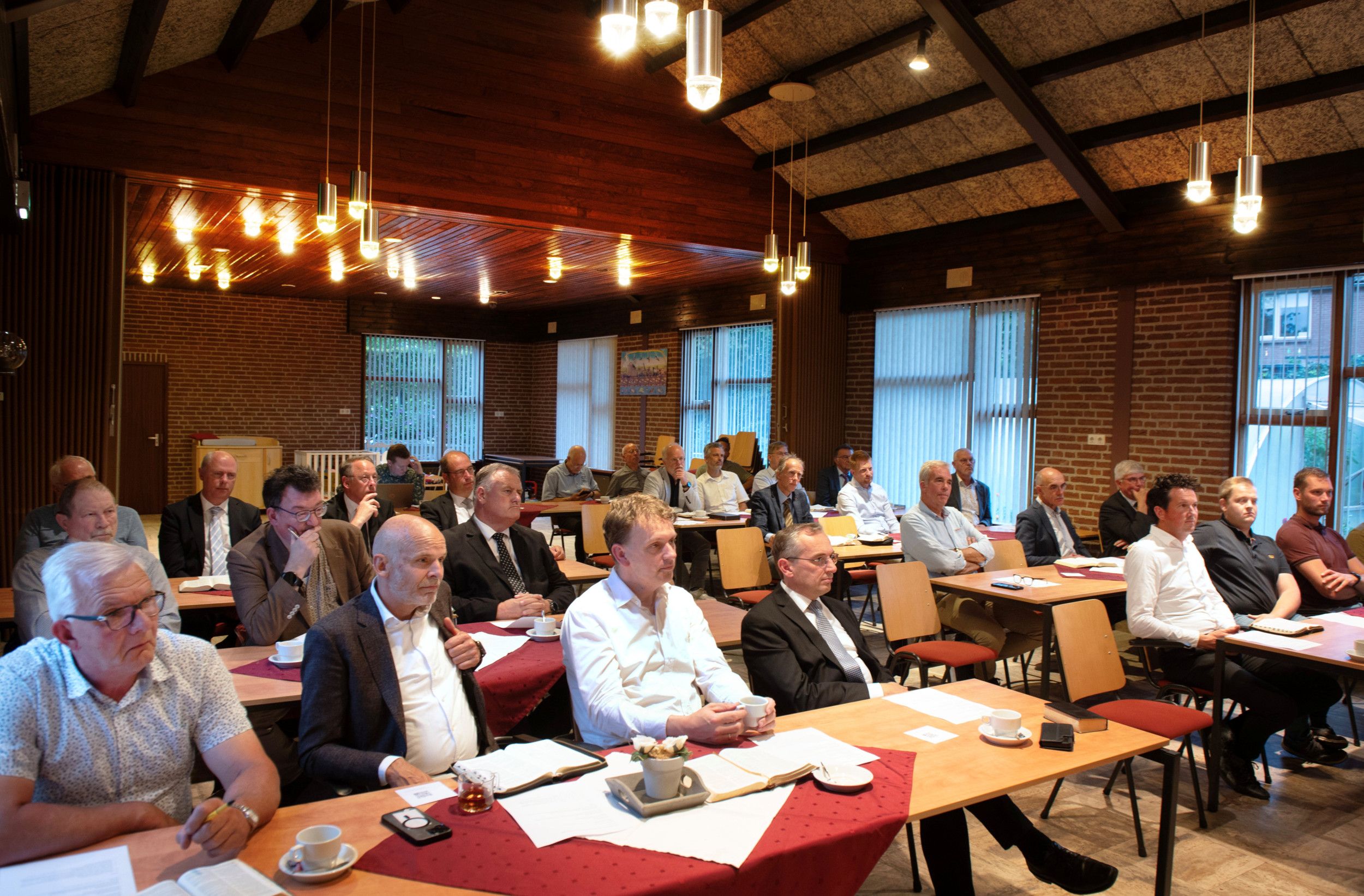 Ambtsdragers van de Gereformeerde Bond in een zaal.