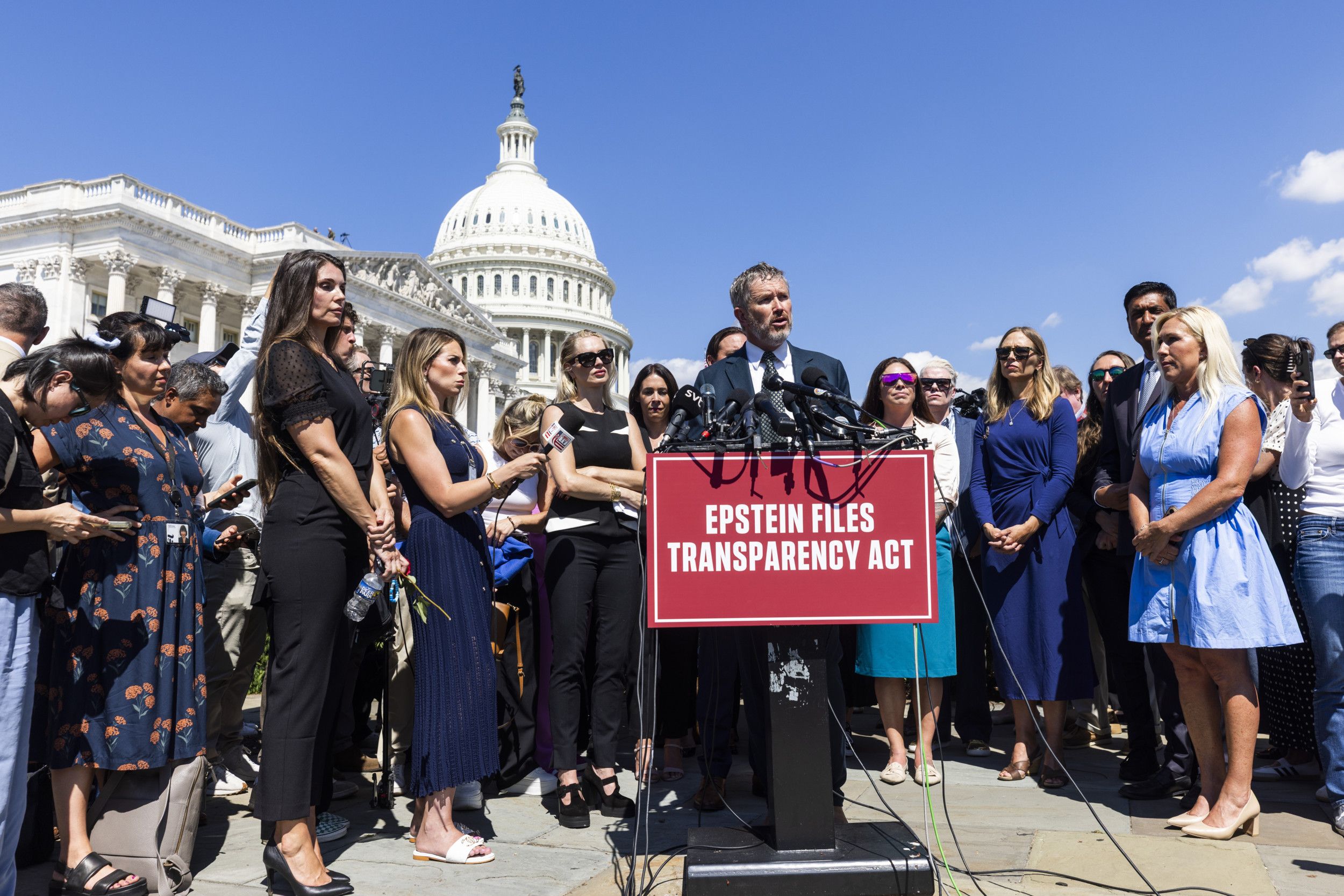 Een man staat voor een spreekgestoelte. Achter hem staan mensen. Daarachter is de koepel van een wit neoclassicistisch gebouw zichtbaar. Het is zonnig weer. 