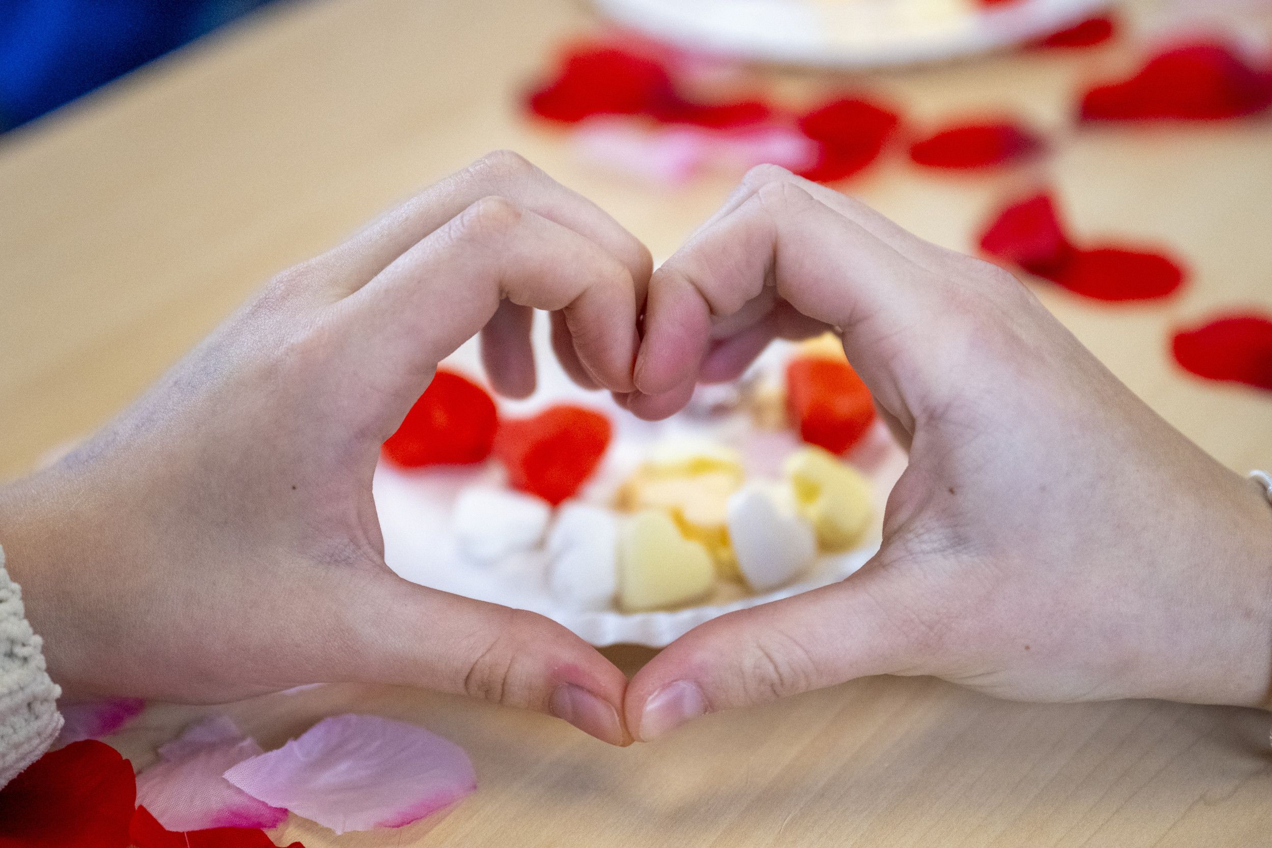 Twee handen maken een hartjesvorm. Op tafel liggen snoephartjes en rozenblaadjes.