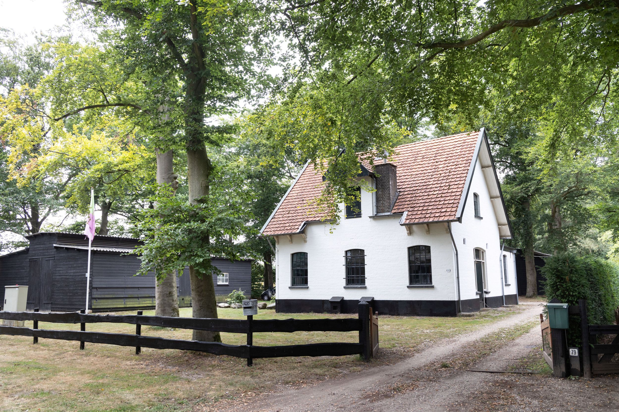 Woning met schuur onder bomen en achter een toegangshek