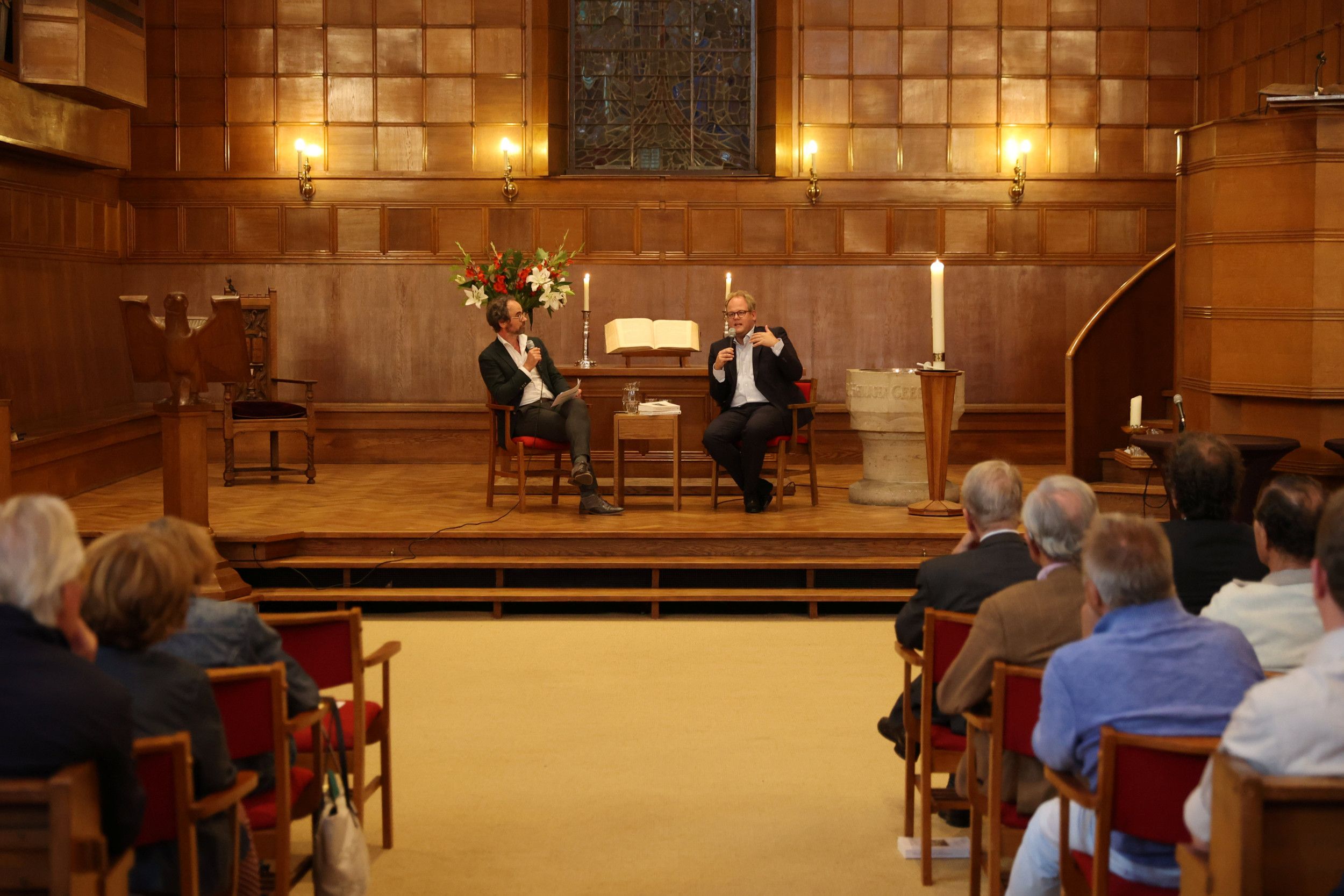 Twee mannen, donker colbert, in gesprek op het podium.