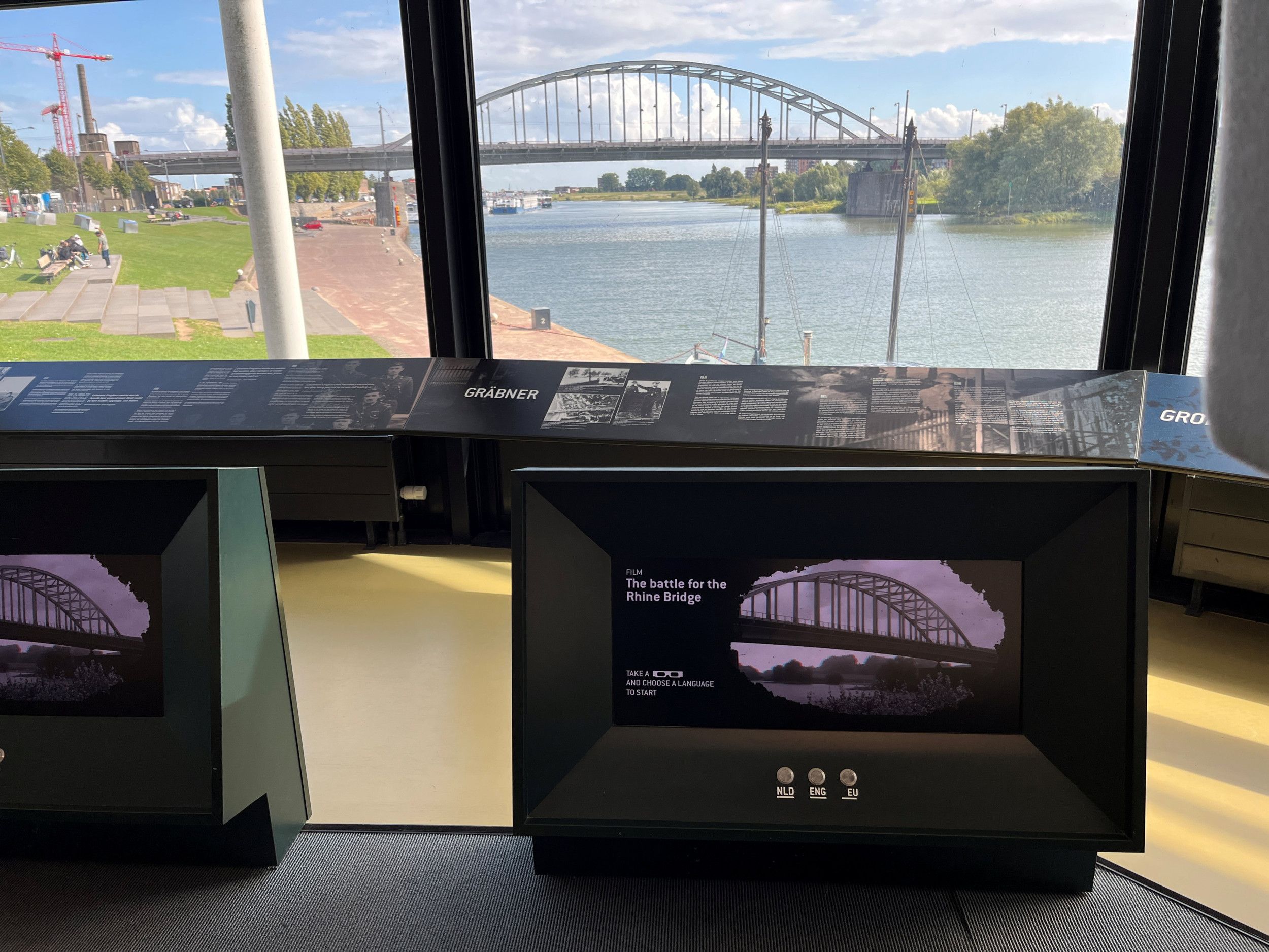 Scherm met film over de brug die je door de ruiten op de achtergrond ziet.