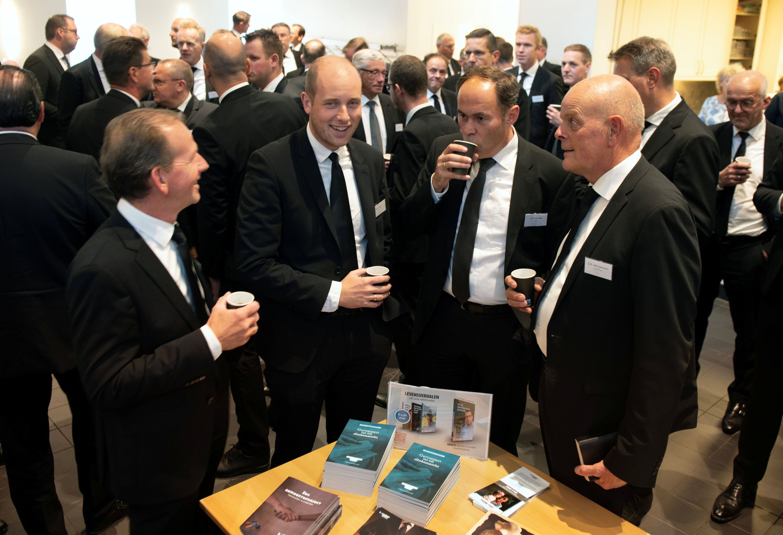 Lachende mannen drinken koffie bij lectuurtafel.