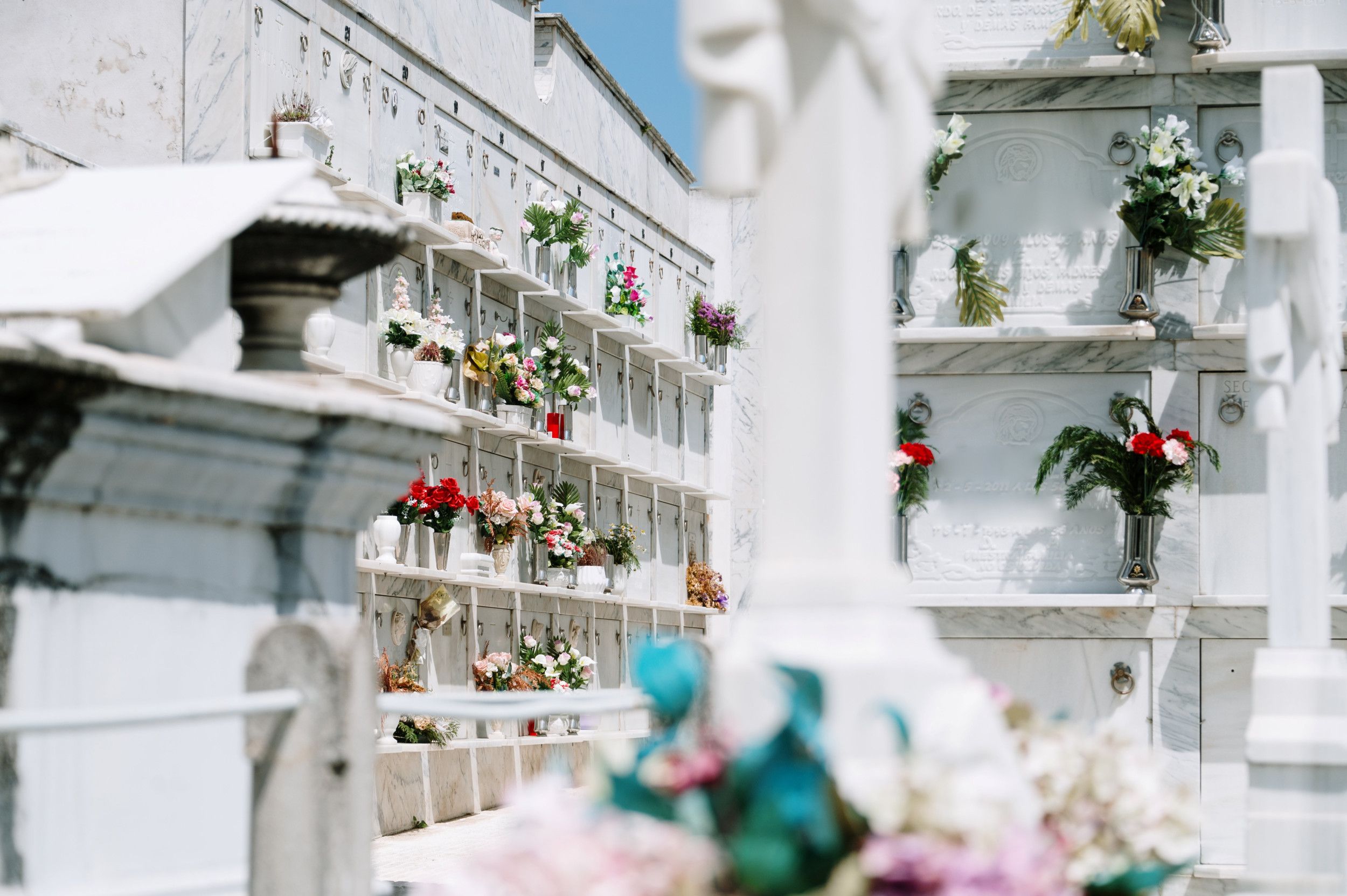 Grafnissen in een witte muur versierd met bloemen en steengravures op een begraafplaats in Spanje.