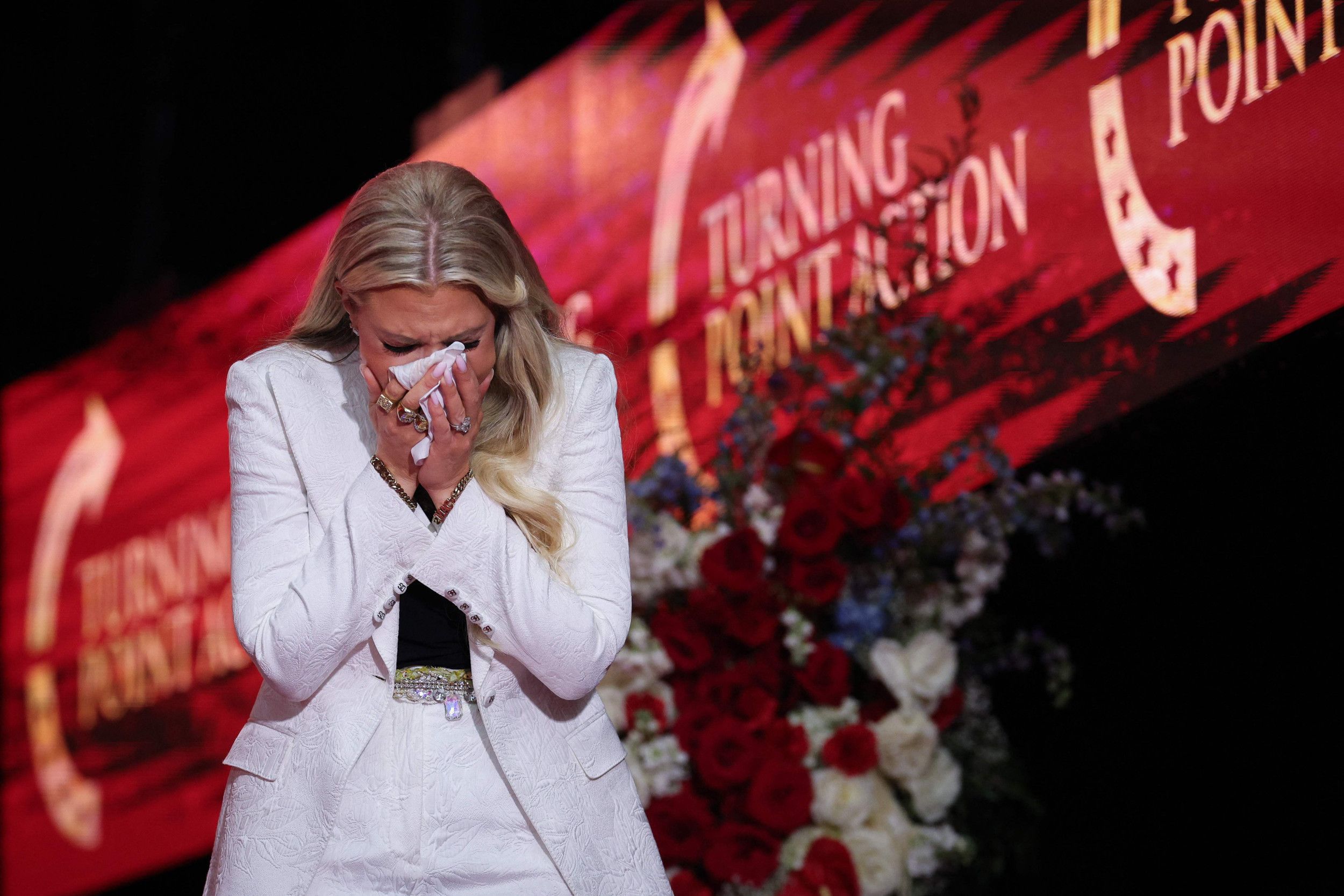 Vrouw in witte kleding houdt met twee handen een witte zakdoek voor haar gezicht.