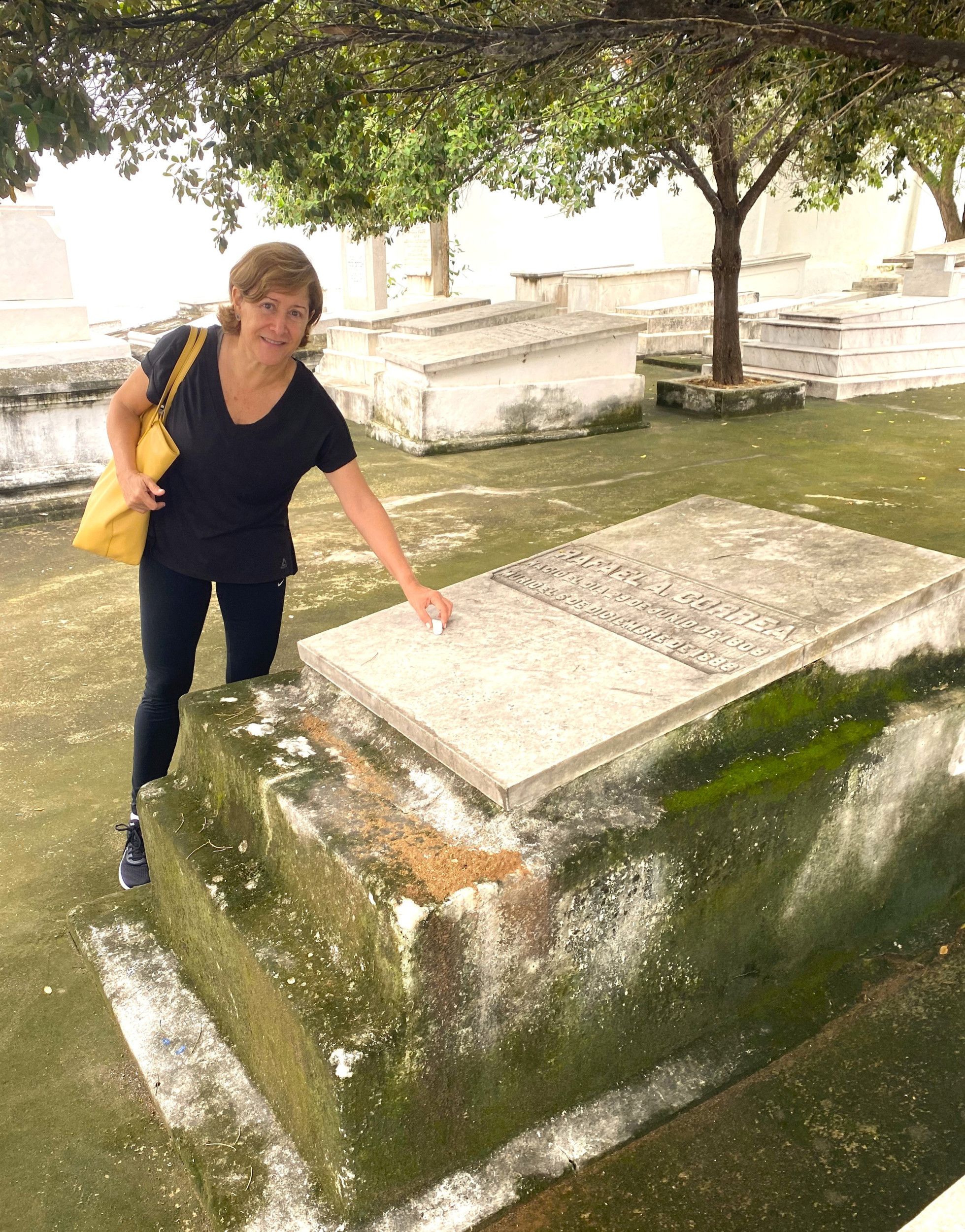 Een oudere vrouw in zwarte vrijetijdskleiding bij een graf dat niet heel wit meer is.