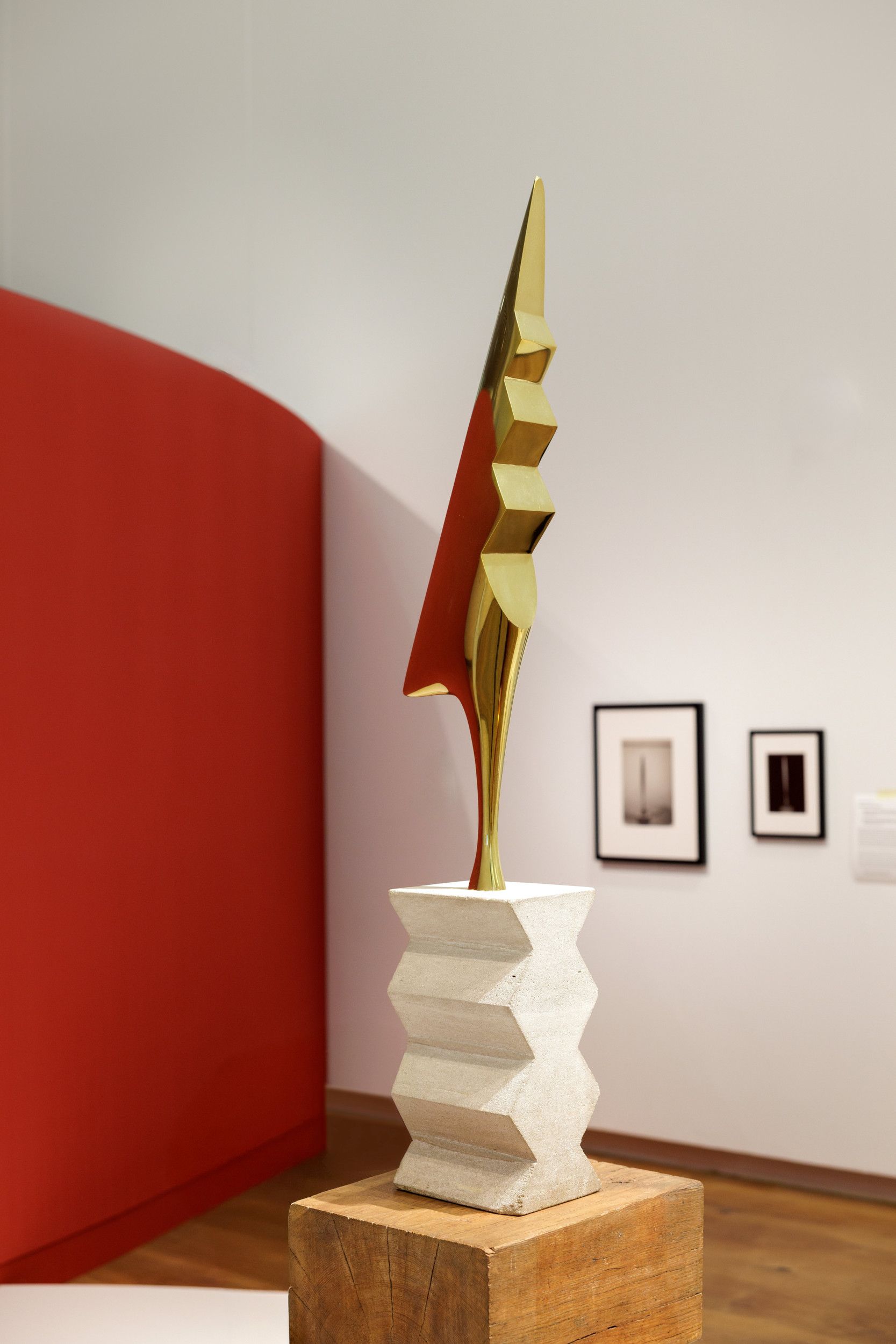 Een slank bronzen beeld met spits staat op een witte gekartelde sokkel van kalksteen.