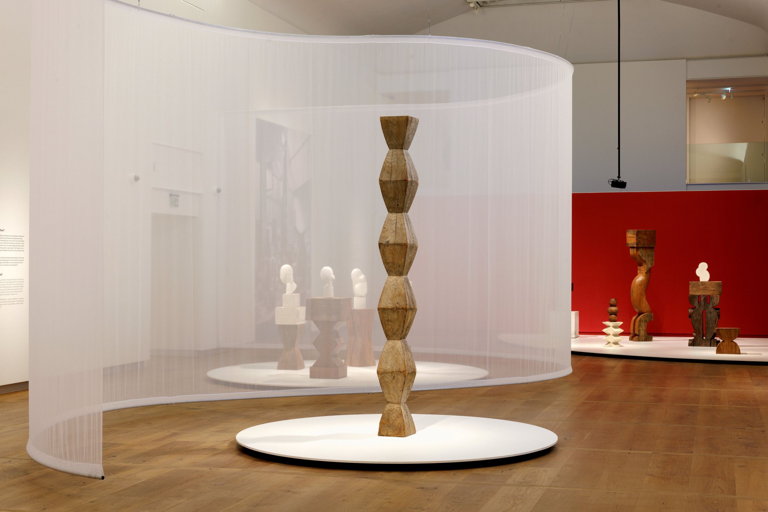 Overzicht van een museumzaal met in het midden een houten kolom met een ruitvorm in herhaling.