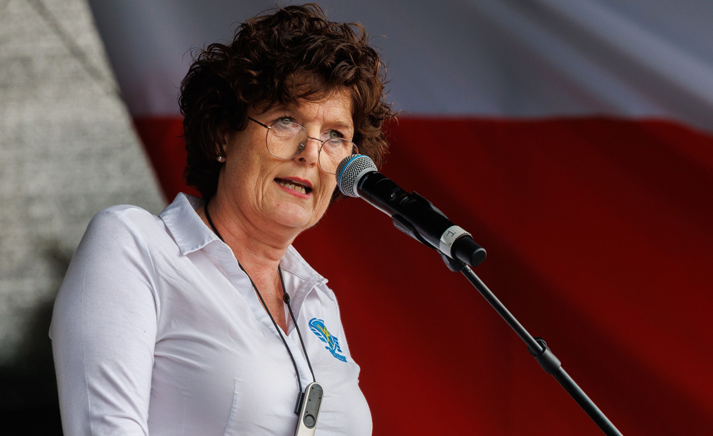 Vrouw met krullend haar en bril spreekt in een microfoon.