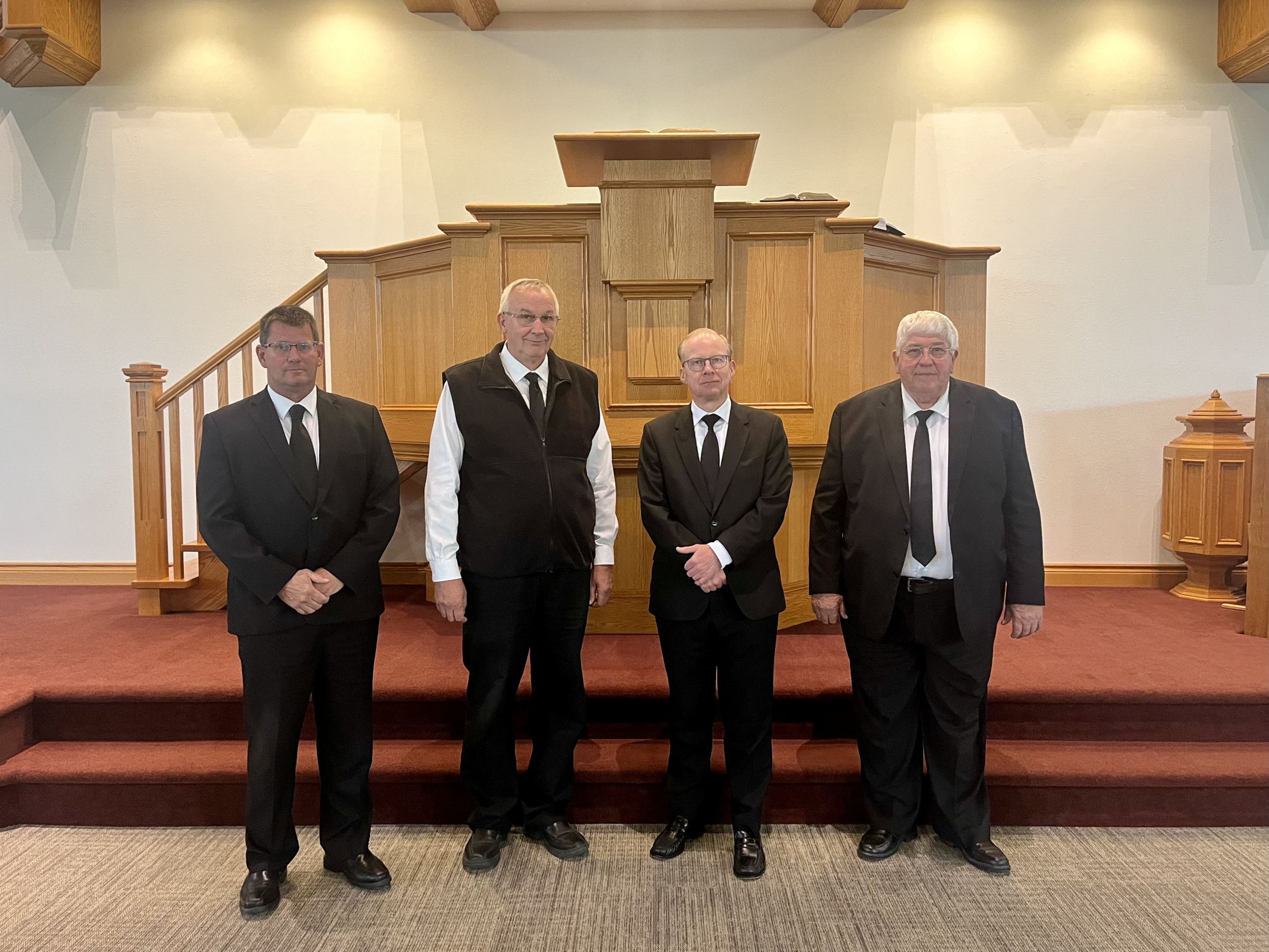 Vier mannen in zwarte pakken voor een preekstoel.