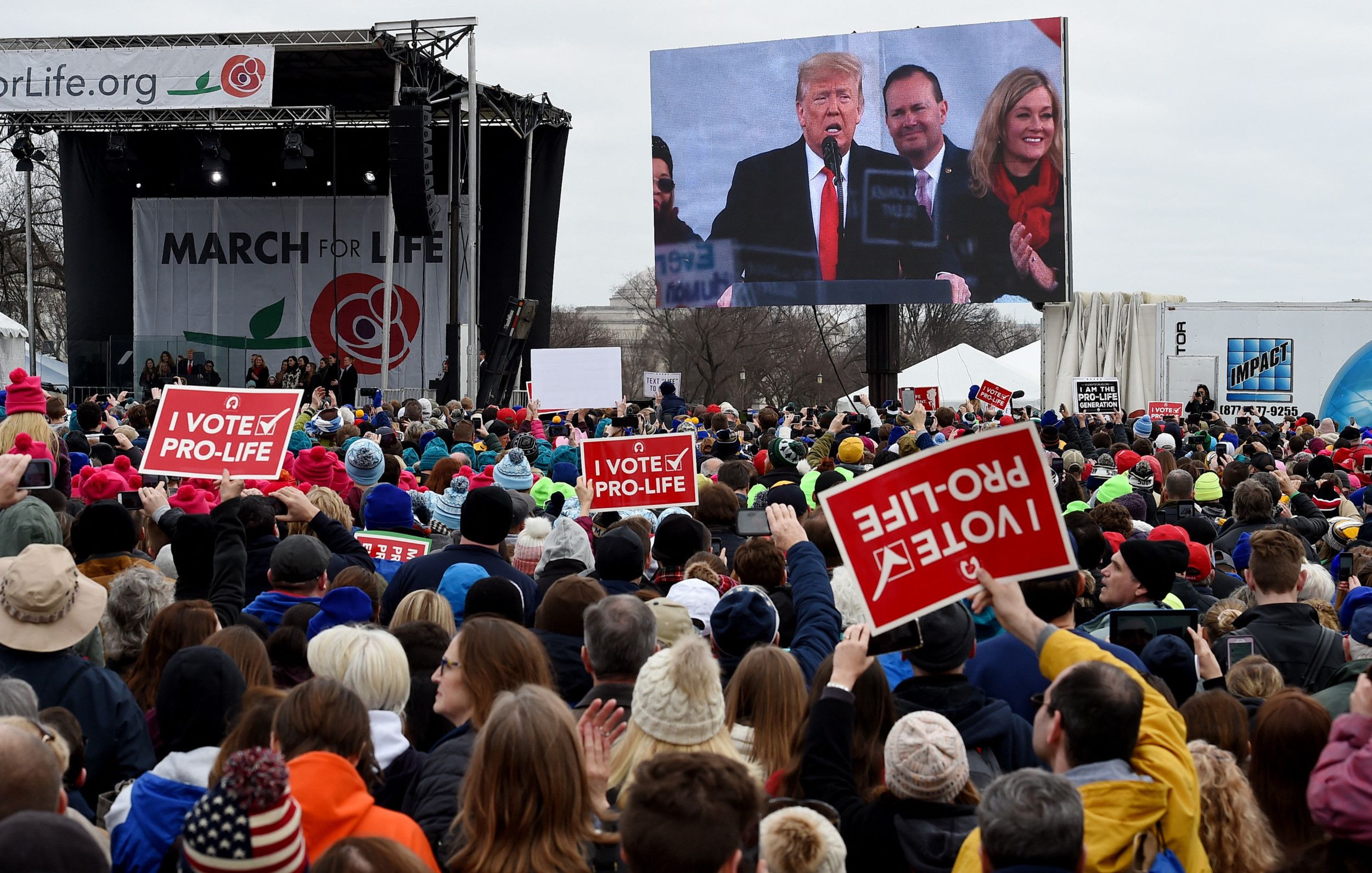 Menigte mensen met borden met ”Ik stem prolife” erop; voorin de Amerikaanse president zichtbaar op een groot scherm.