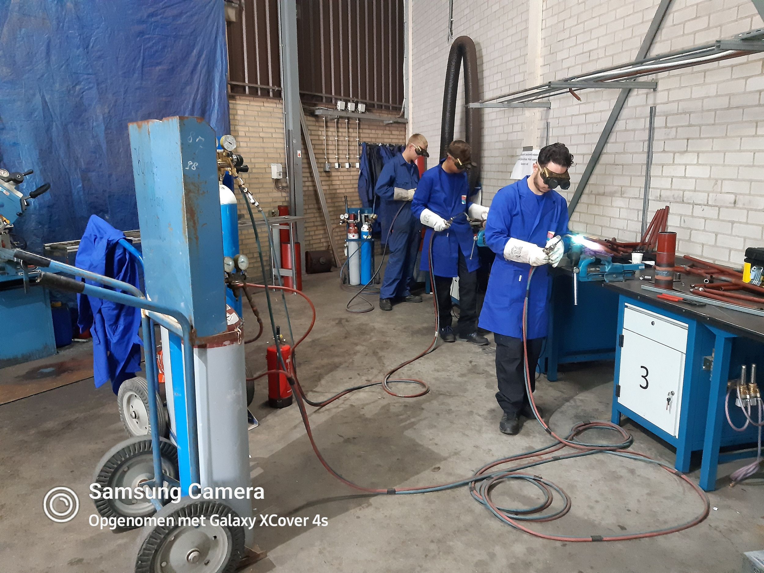 Drie jongens lassen in een werkplaats. 