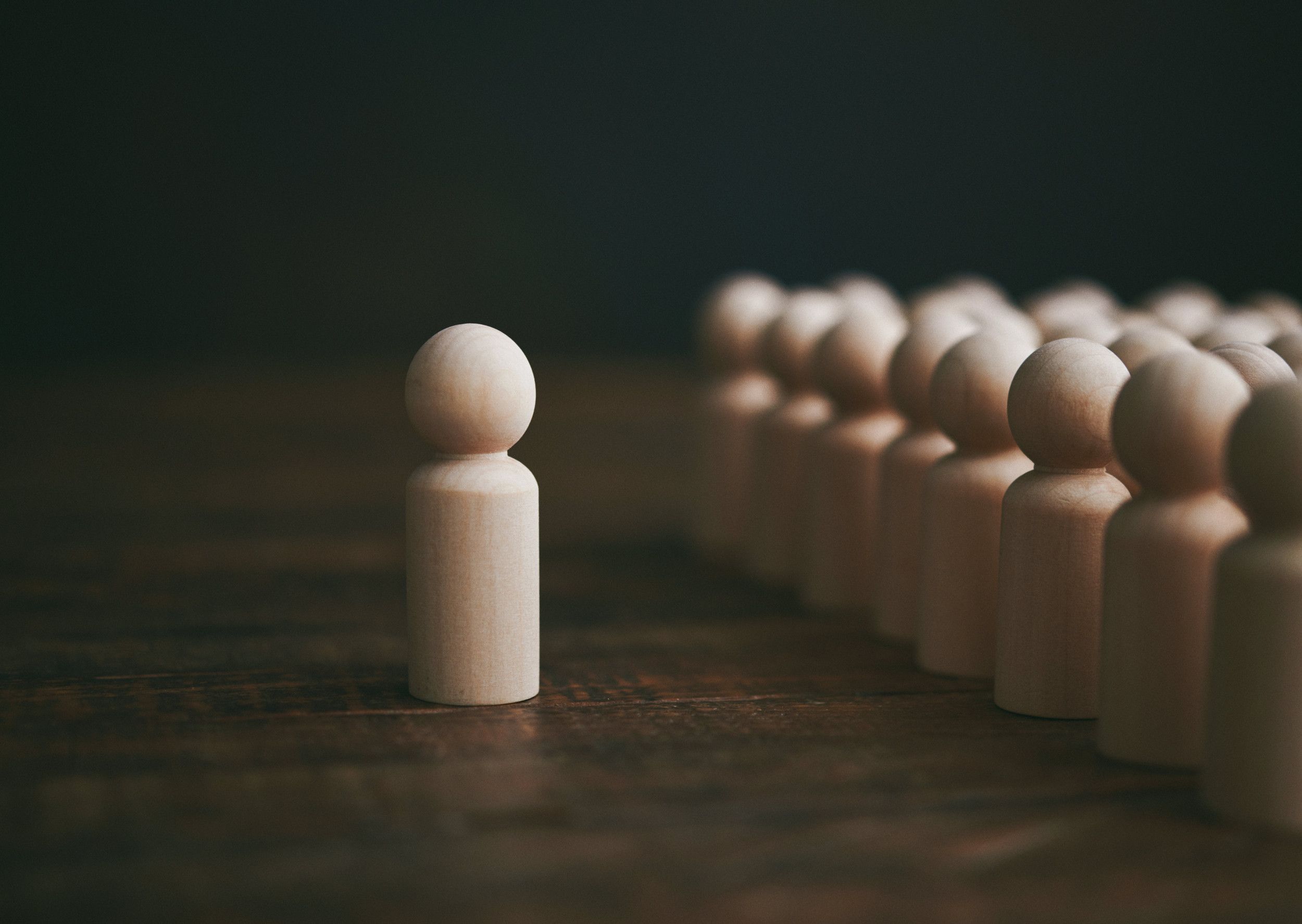 Verzameling van generieke houten figuren in de vorm van mensen met een figuur die buiten de groep staat.