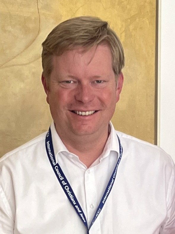 Man met blond haar in wit overhemd met keycord om zijn nek.