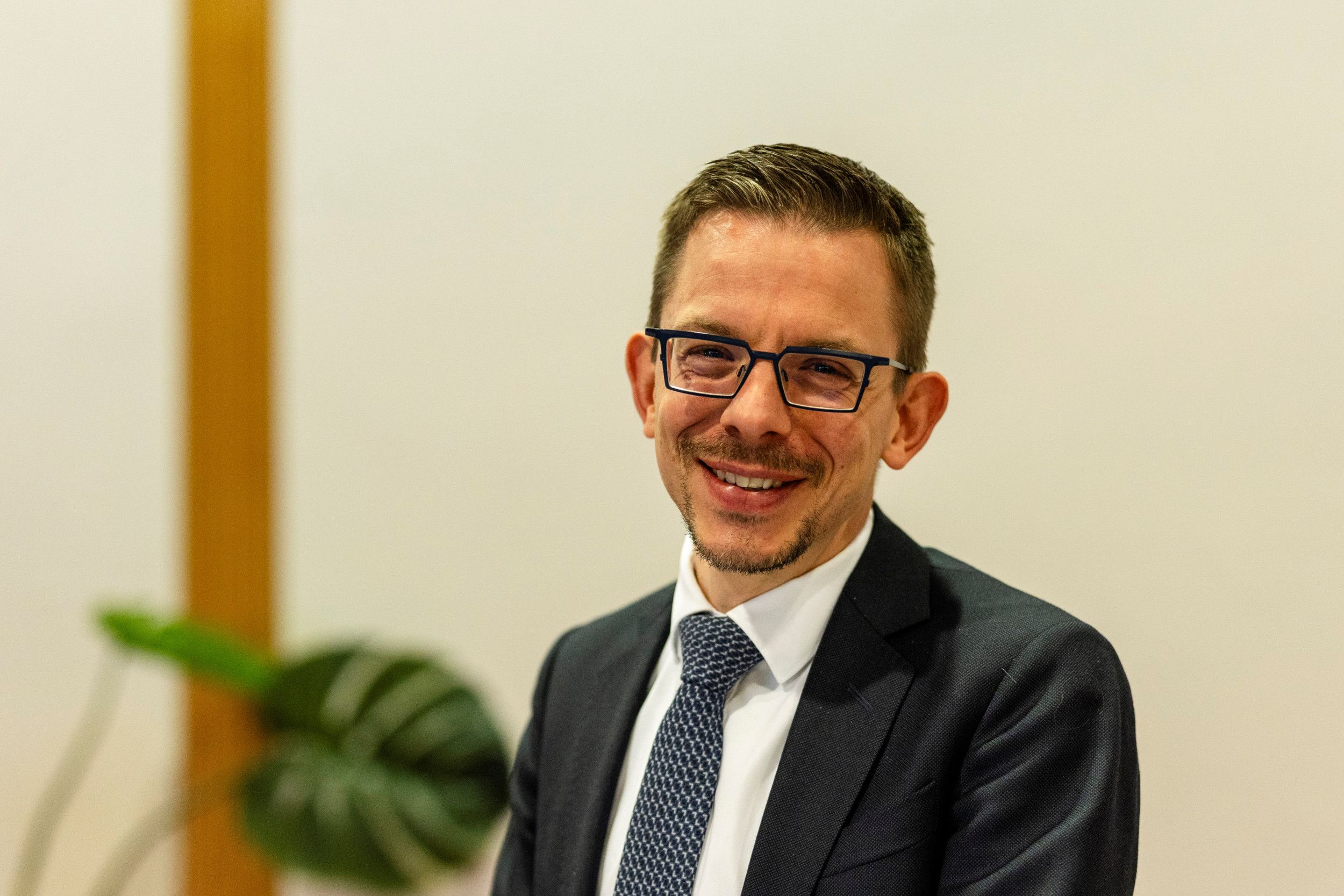 Man in donker pak, lachend, met das, bril en klein baardje.