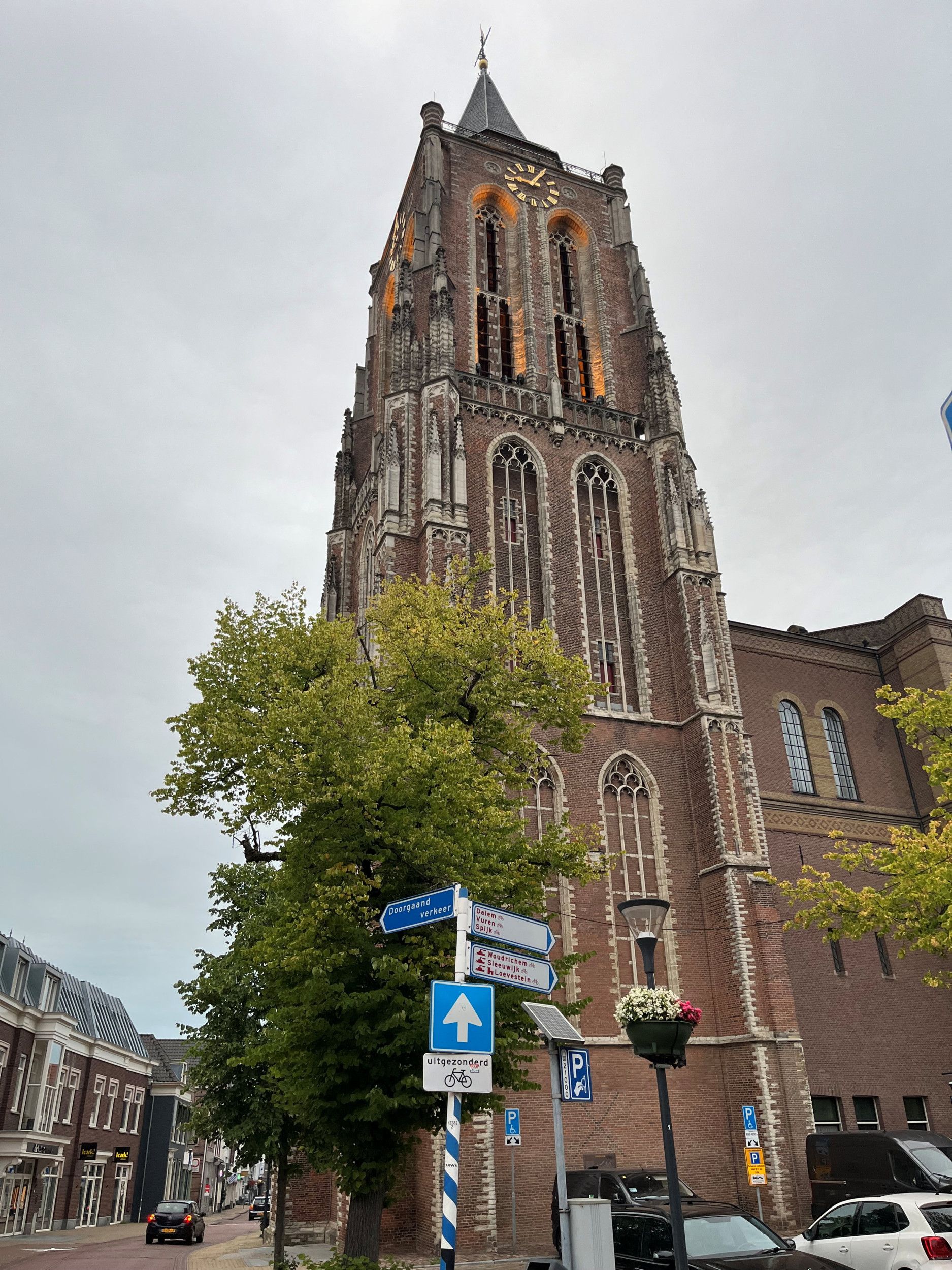 Een hoge kerktoren, op de voorgrond een richtingwijzer met plaatsnaamborden.