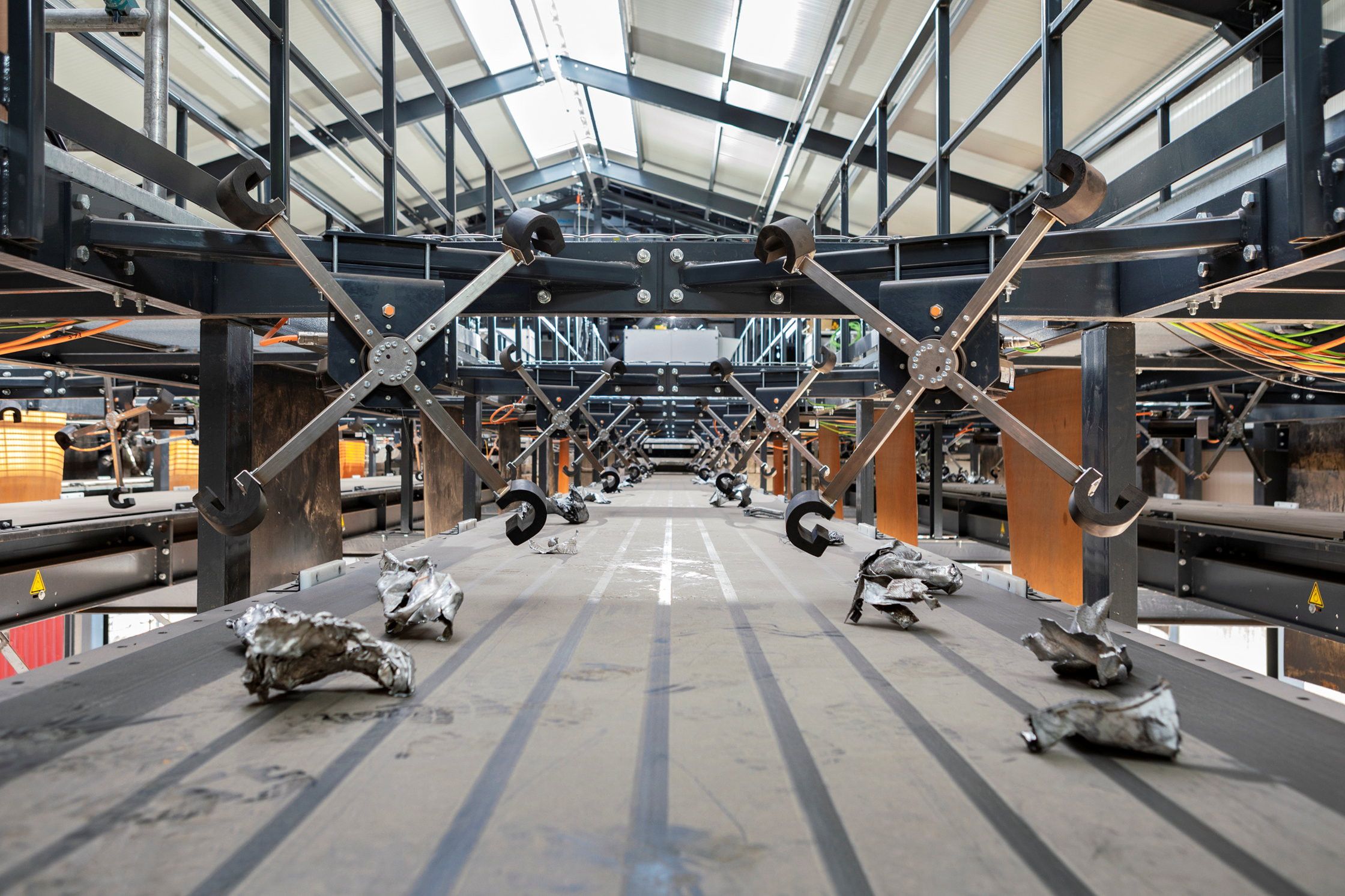 Op een lopende band liggen stukjes schroot. Er boven hangen een soort molenwieken die de schrootstukjes van de band kunnen tikken. 