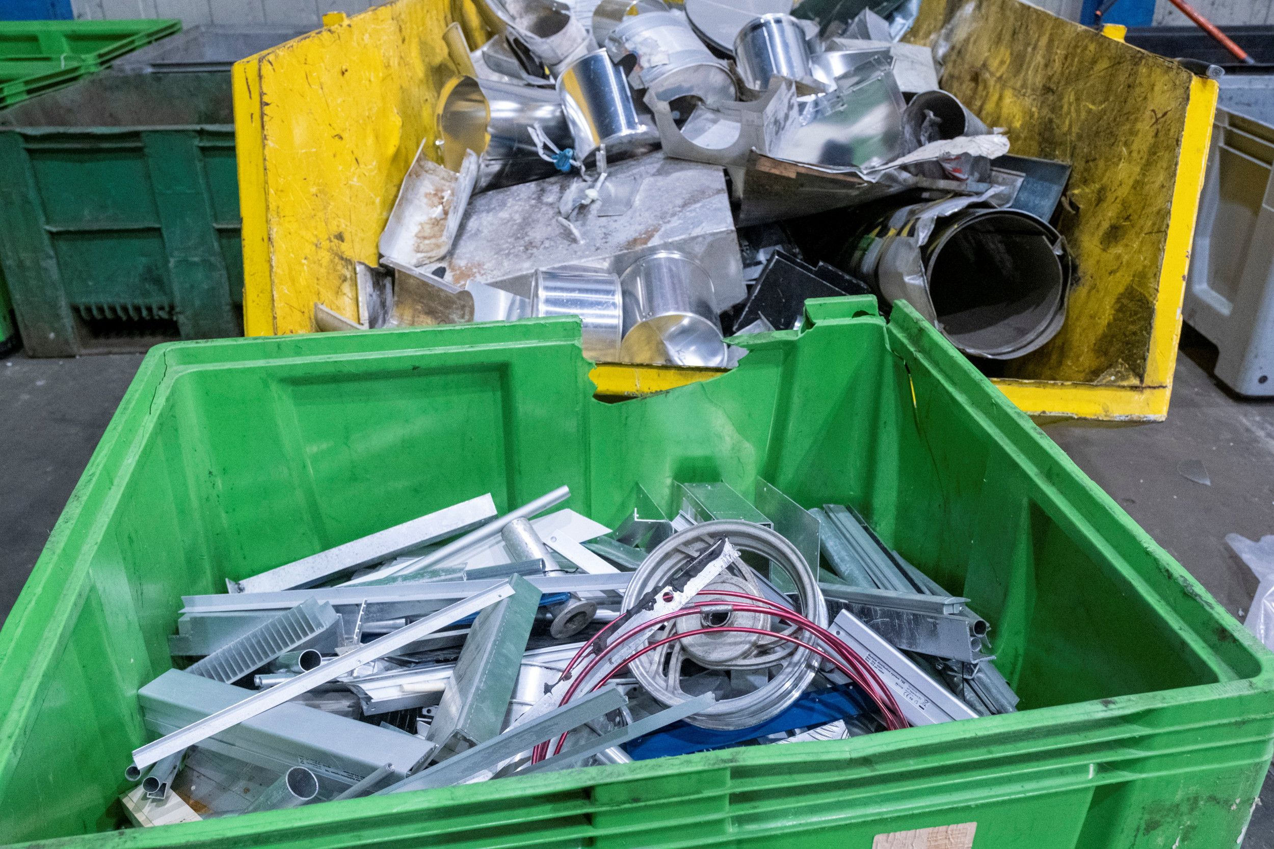 Een groene bak op de voorgrond en een gele bak erachter zitten allebei vol oud ijzer. 