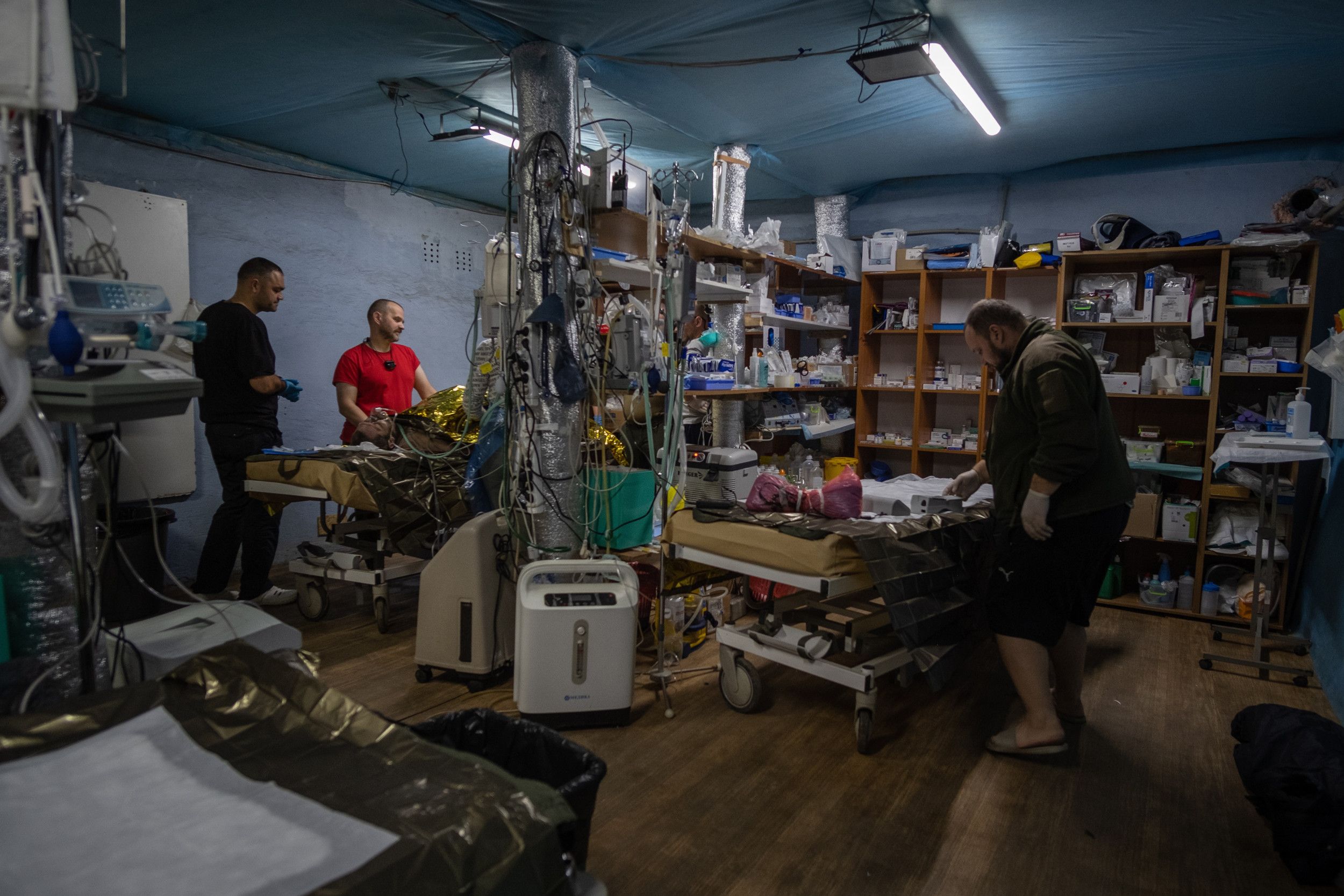Ruimte met stellingen met medicijnen en twee bedden. Op een daarvan ligt een man, met over hem heen een reflecterende reddingsdeken.