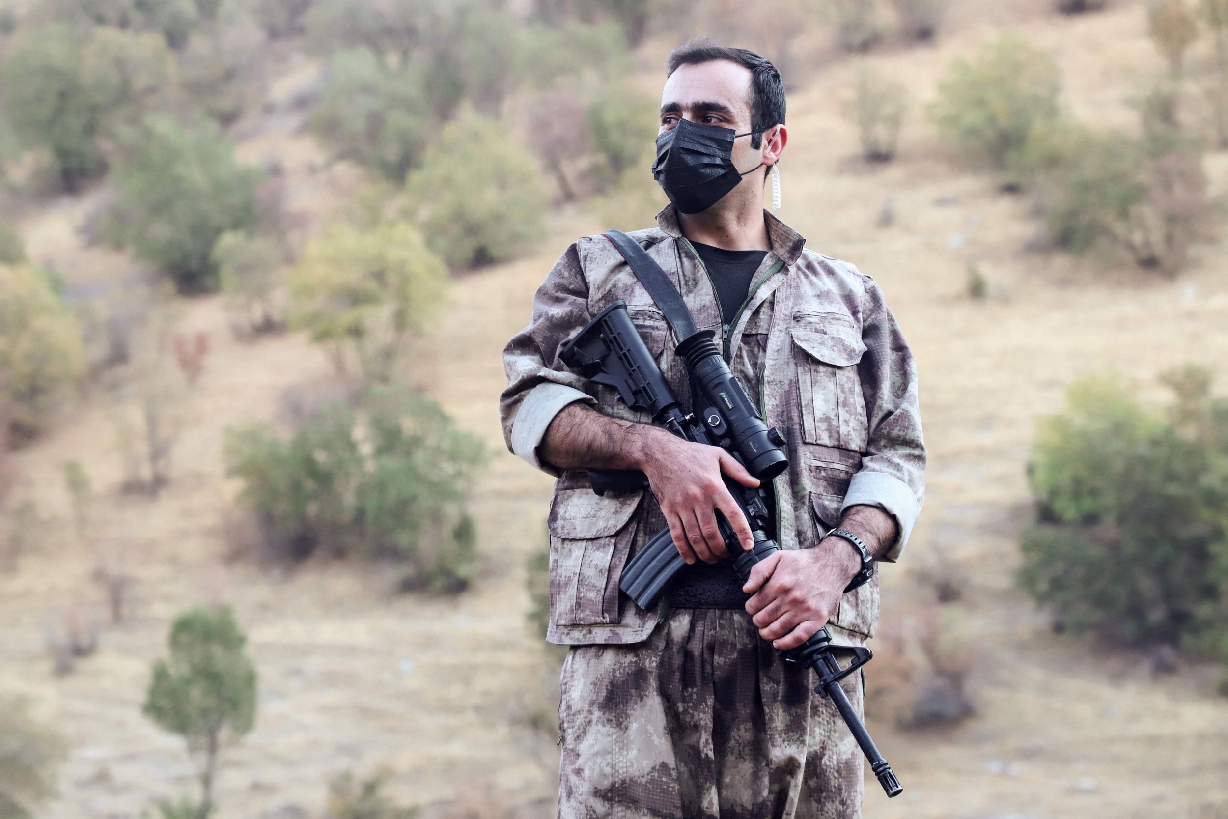 Man in grijze camouflagekleding houdt met twee handen een geweer vast.