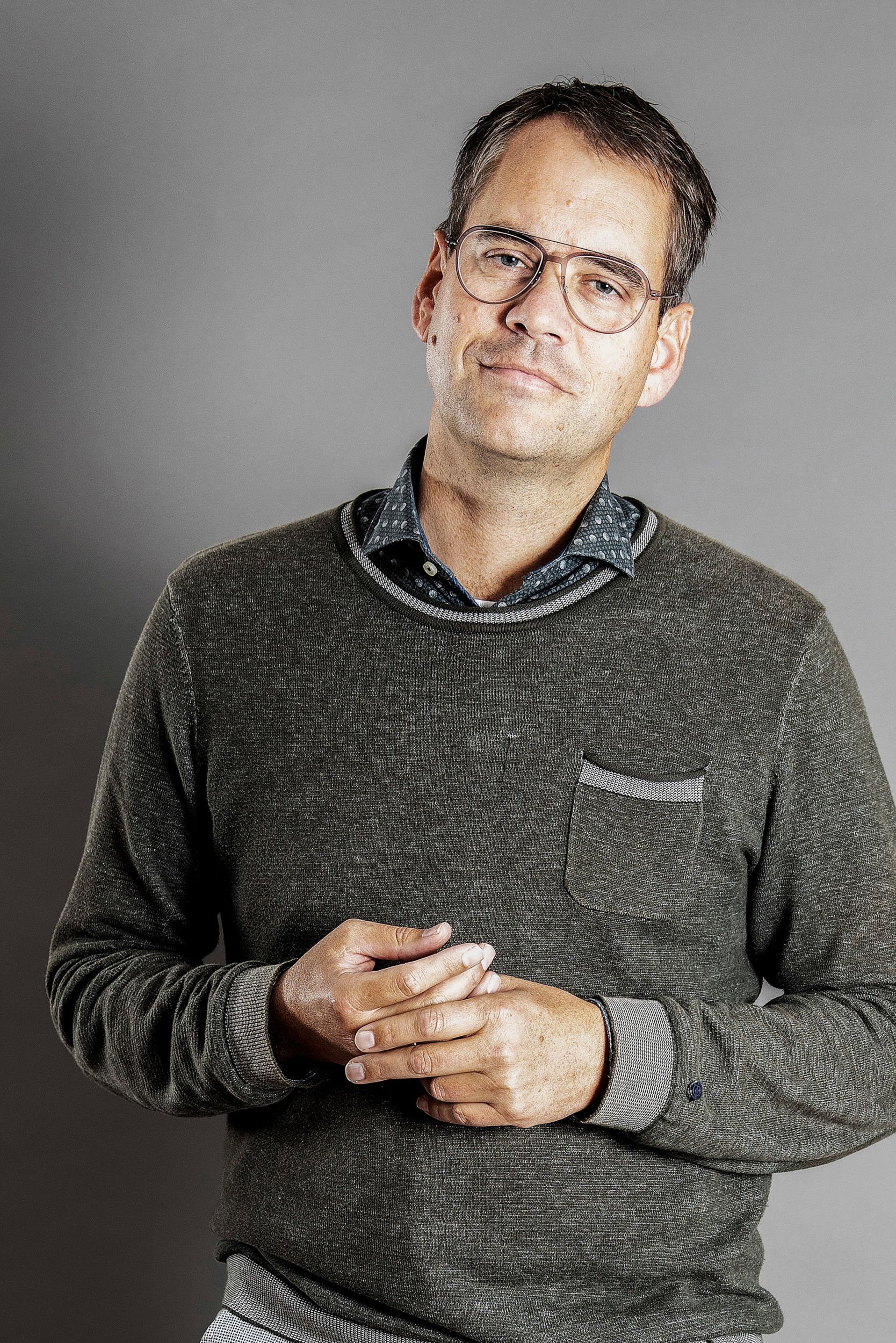 Man met bril in grijze trui kijkt rustig in de camera.